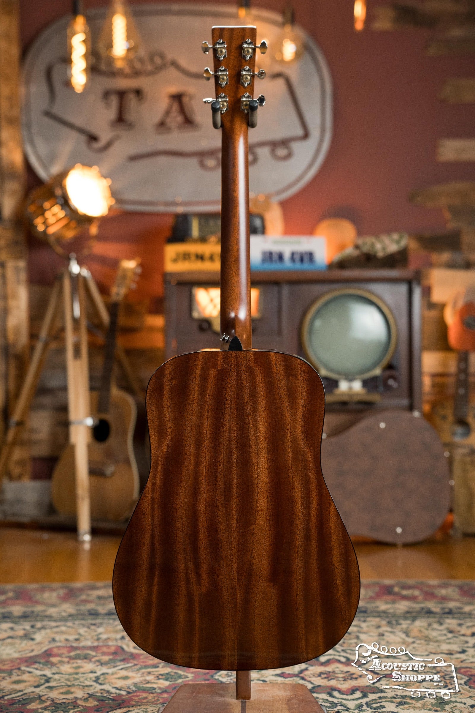 A Martin & Co. DE Retro Plus Torrefied Spruce/Mahogany Dreadnought Guitar with Martin Electronics (#0808) stands upright, back view, in a cozy vintage-themed room with retro decor, warm lighting, musical instruments, and a patterned rug.