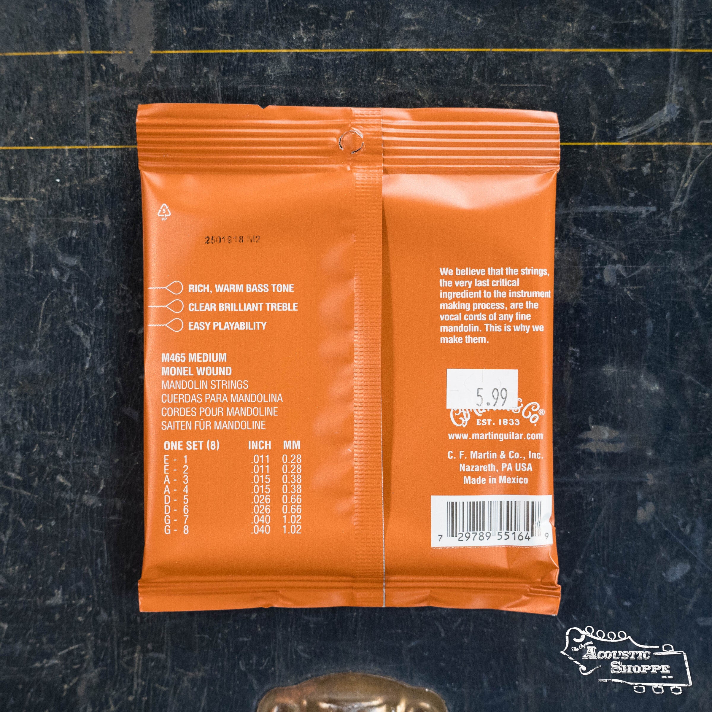 An orange packet of Martin & Co. Medium Mandolin Strings Monel 41Y18M465 rests on a dark surface, showing string gauges, a $5.99 price tag, and the Martin & Co. logo—offering a rich, resonant tone for your mandolin.