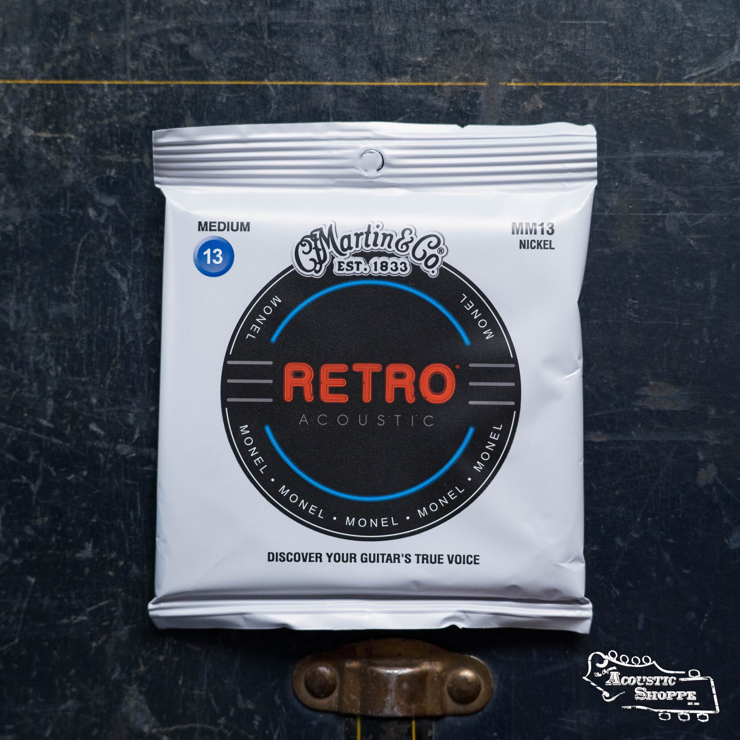 A sealed pack of Martin & Co. Martin Retro Medium Acoustic Guitar Strings 41Y19MM13 lies on a worn dark surface, with The Acoustic Shoppe logo visible in the corner.
