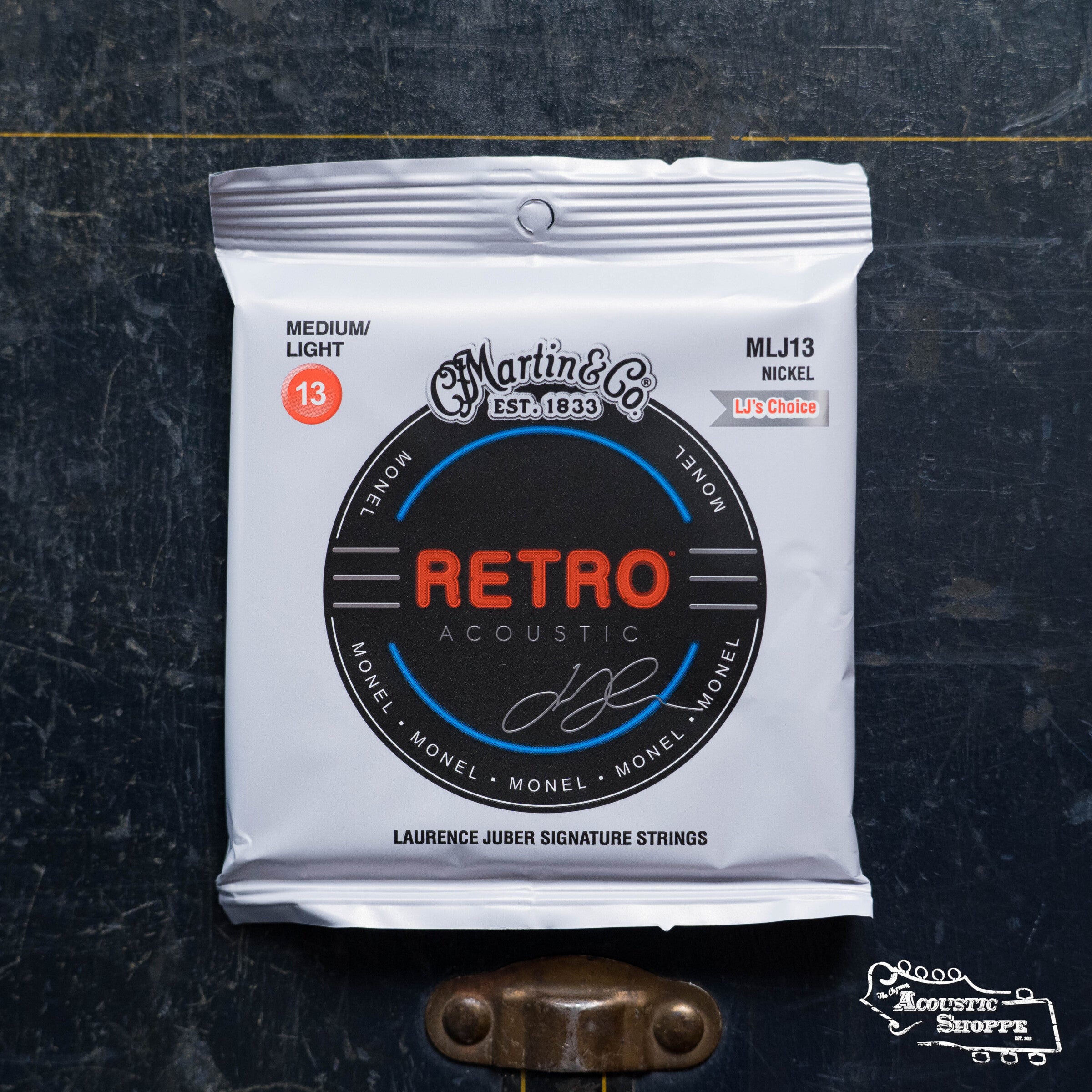 A pack of Martin & Co. Retro Medium/Light-LJ's Choice Acoustic Guitar Strings (41Y19MM13) rests on a dark textured surface, with "Medium/Light" noted on the silver packaging.