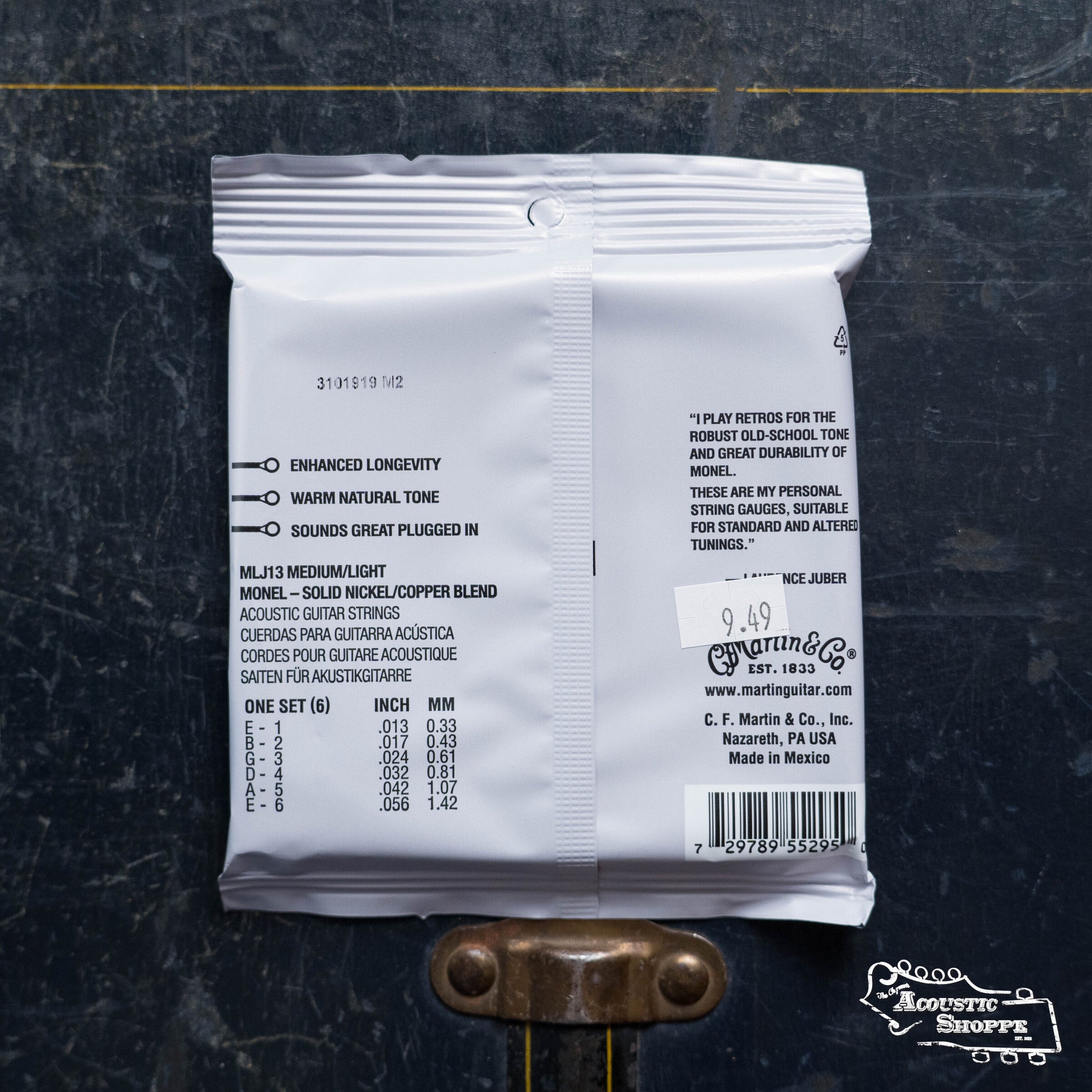 Back of a white Martin & Co. Martin Retro Medium/Light-LJ's Choice Acoustic Guitar Strings 41Y19MM13 package, showing Monel wrap wire details, barcode, price sticker, benefits list, and description on a dark wood surface with metal hardware below.