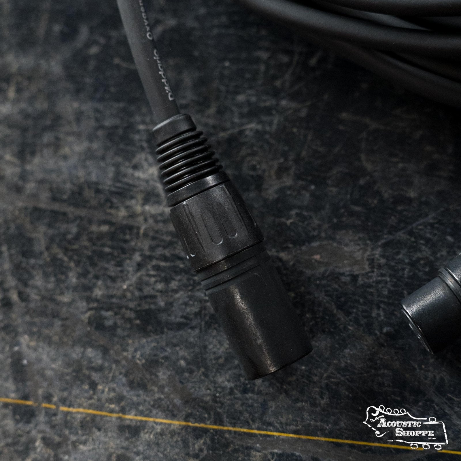 A close-up of the D'Addario Classic Series XLR Microphone Cable (50ft, PW-CMIC-50) is coiled on a dark textured surface, with its black connector visible near the center and a small D'Addario logo at the bottom right.