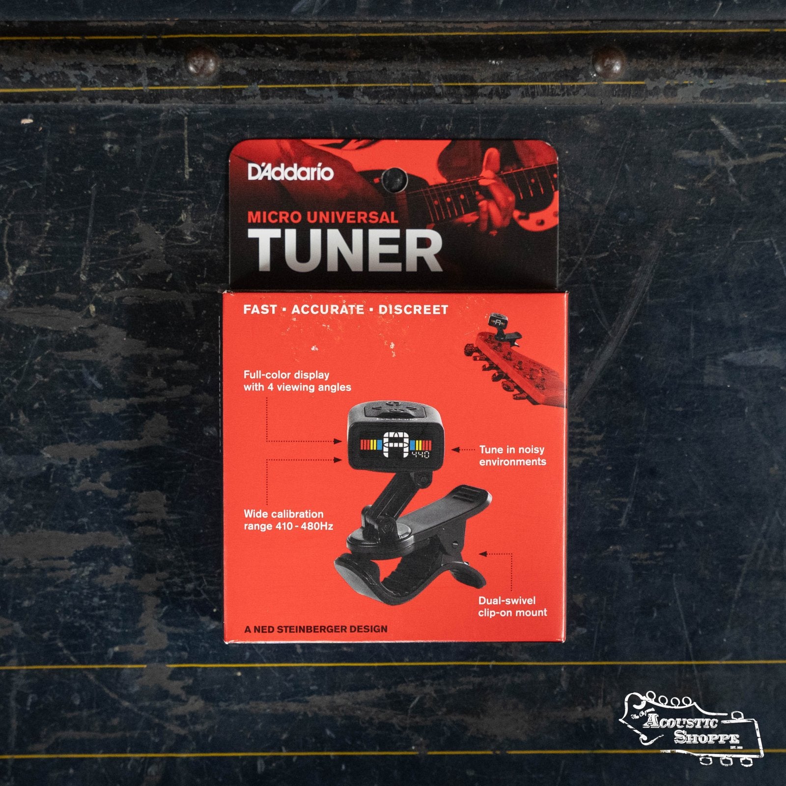 A boxed D’Addario Planet Waves NS Micro Universal Tuner PW-CT-13 rests on a dark textured surface, its red packaging featuring a full-color display, wide calibration range, dual-swivel clip, and advanced piezo transducer.