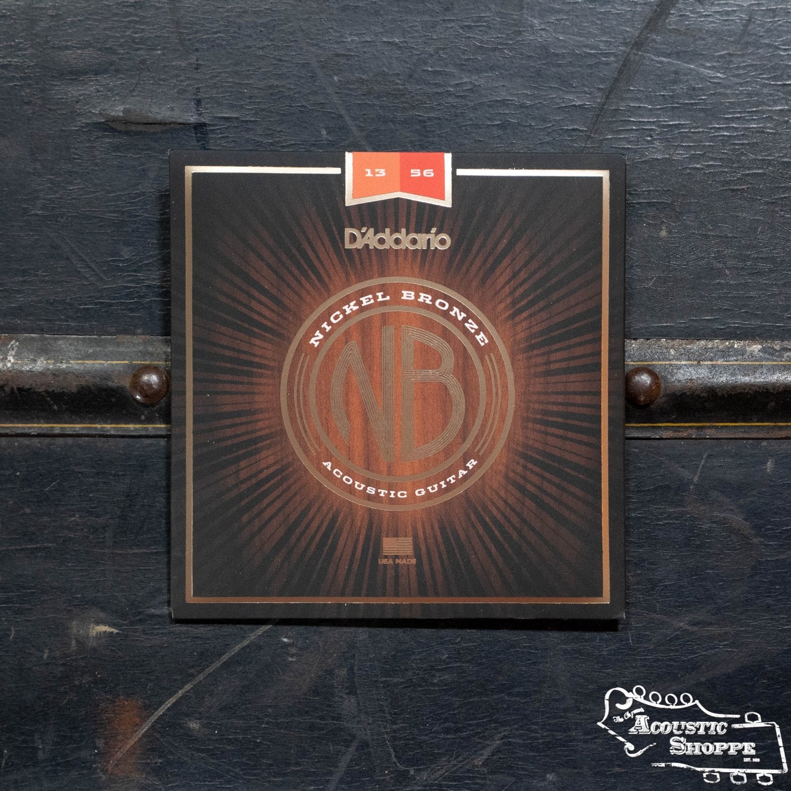 A pack of D'Addario NB1356 Nickel Bronze Acoustic Guitar Strings, Medium 13-56, is shown against a dark textured background with The Acoustic Shoppe logo in the lower right corner.