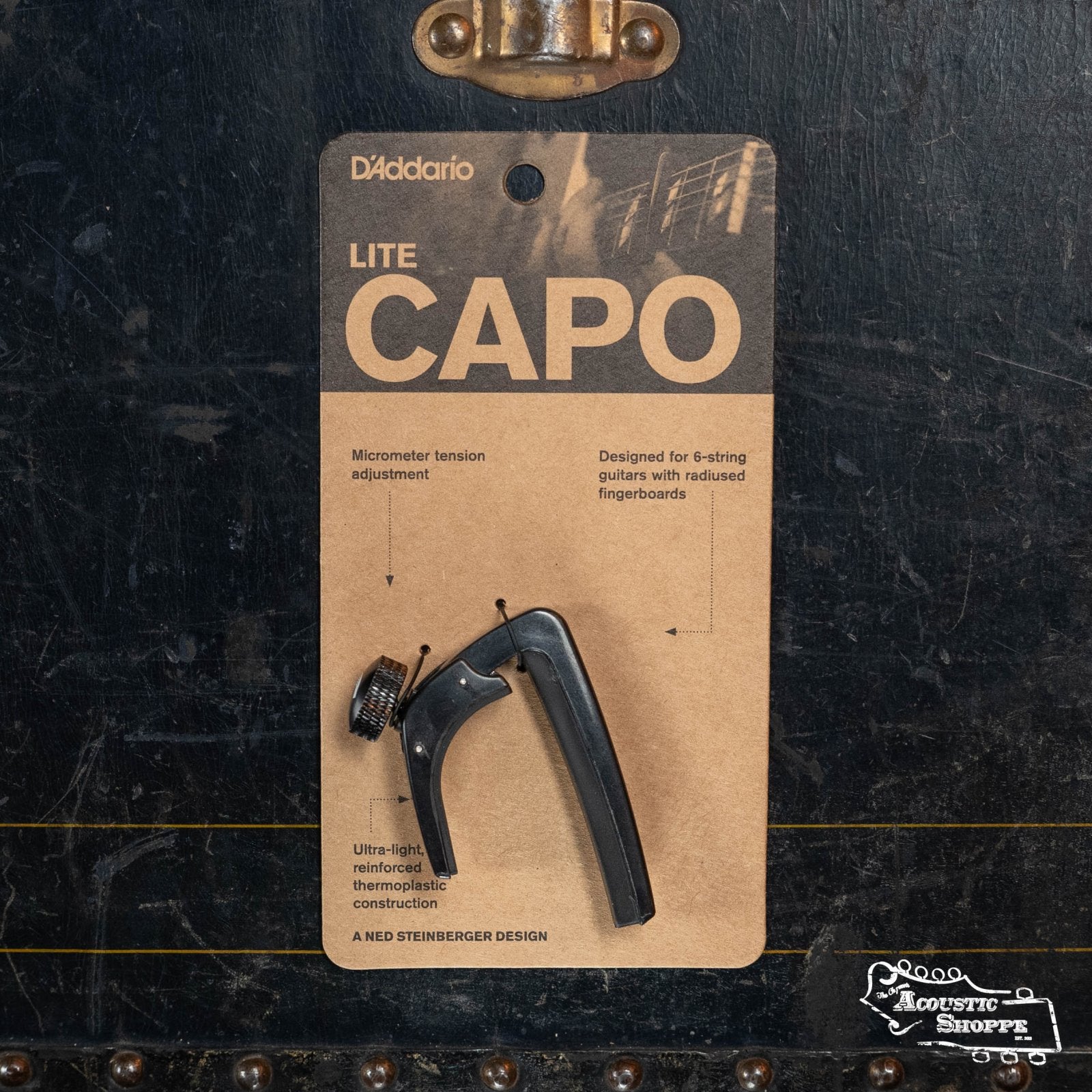 The D'Addario NS Capo Lite PW-CP-07 for 6-string guitars is shown in packaging against a dark background, with features like precise tension control and lightweight design highlighted on the pack.