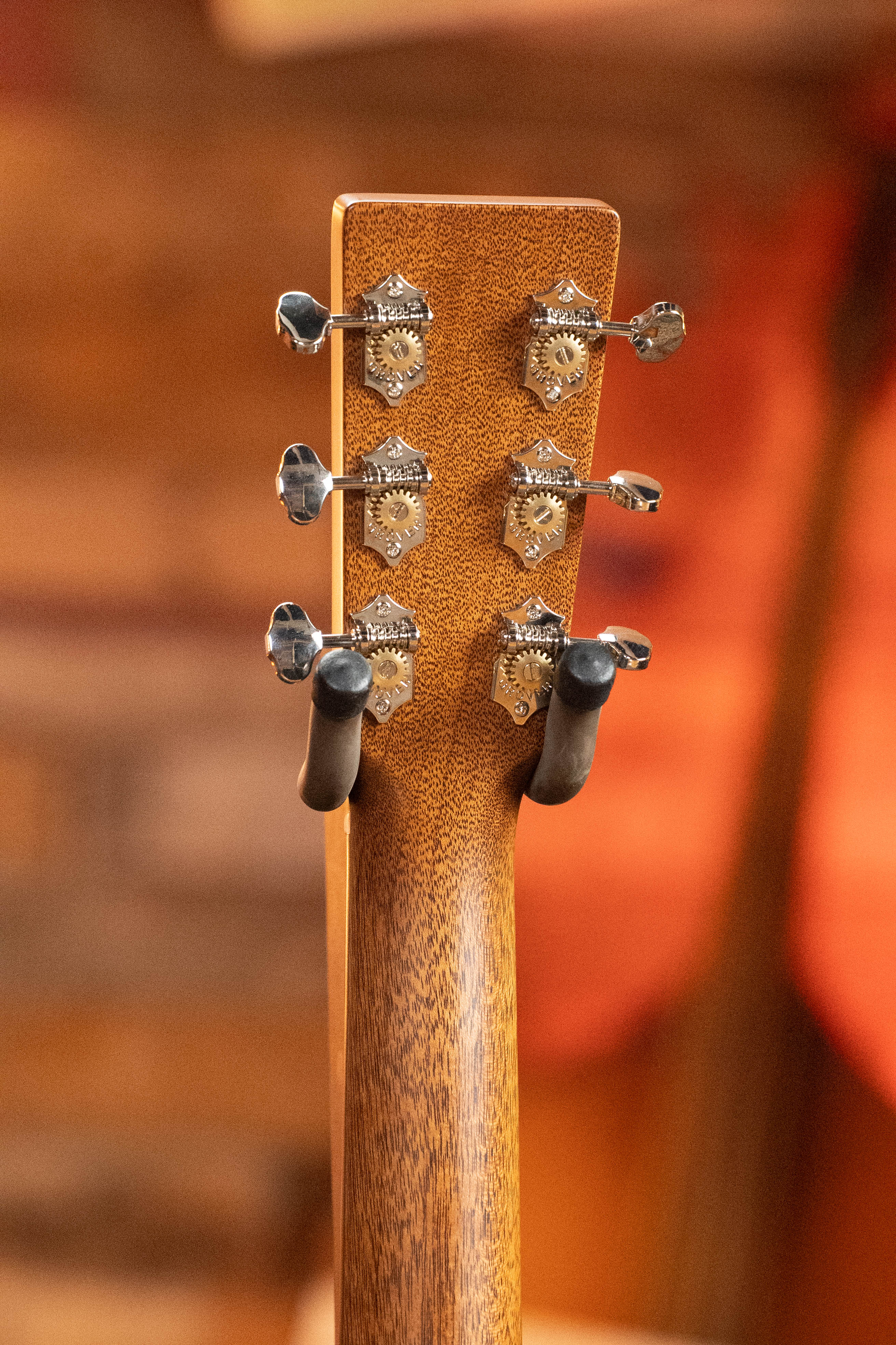 Close-up of the back of a Martin & Co. *New 2025 Model* D-18 1933 Gloss Ambertone Spruce/Mahogany Dreadnought Acoustic Guitar #6784 headstock, showing six tuning pegs and mechanical tuners with a wooden finish and blurred background.