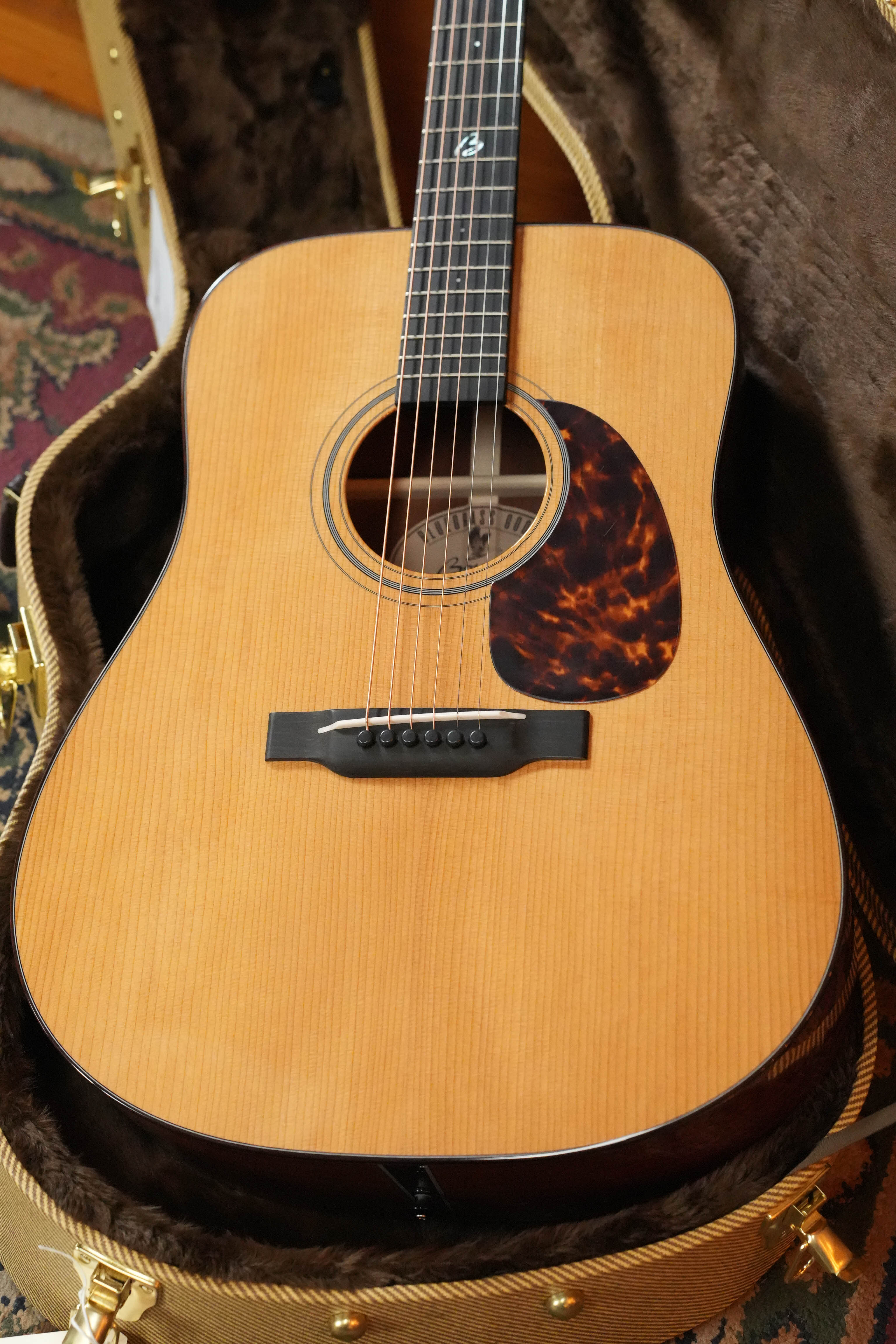 A close-up of the Boucher Guitars *New 2026 Model* BG-42T-G Bluegrass Goose Gold Pack dreadnought acoustic guitar (#1082), featuring a torrefied Adirondack top, torrefied mahogany body, and resting in a padded brown case.