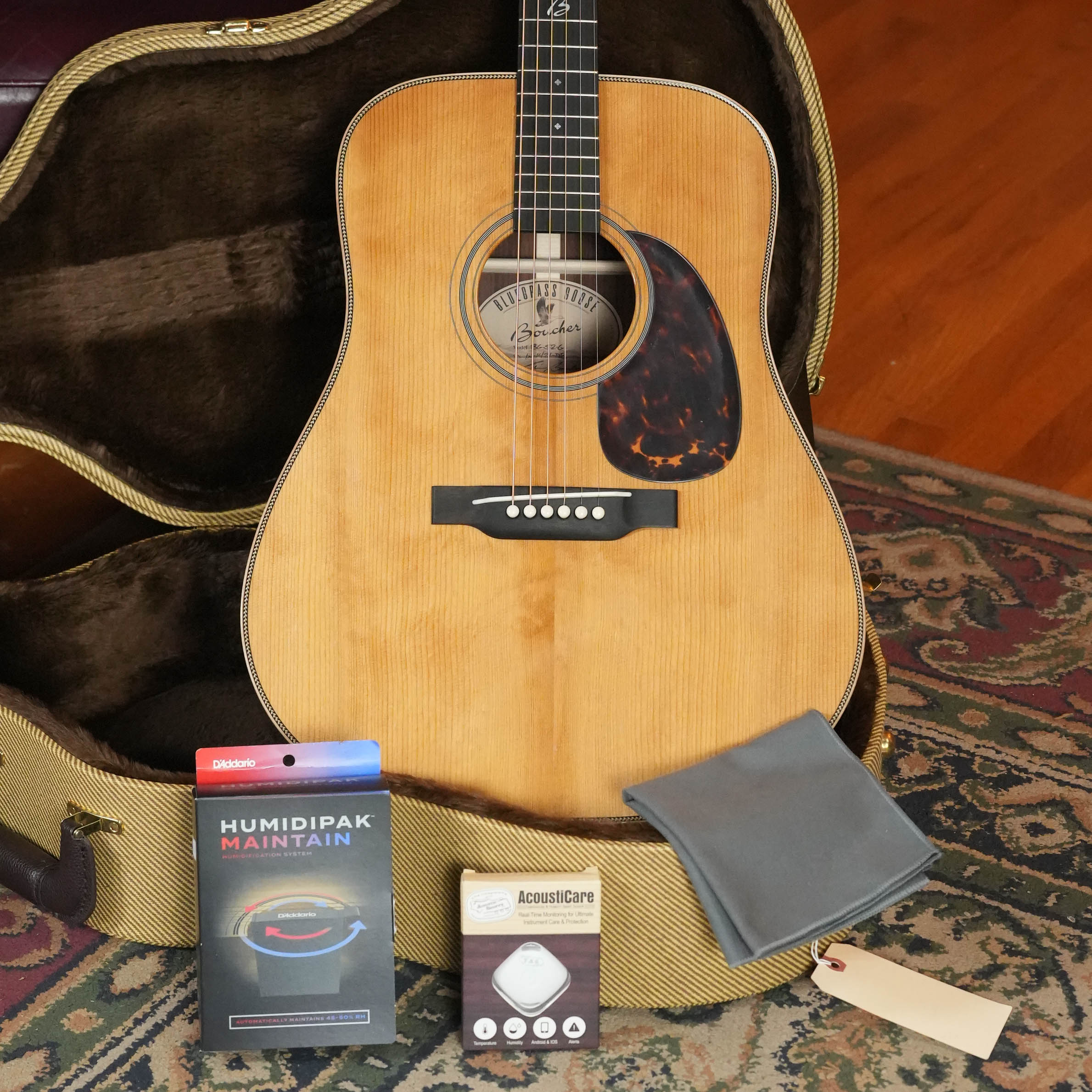 A *New 2026 Model* Boucher BG-52-G Torrefied Adirondack/Rosewood Bluegrass Goose Gold Pack acoustic guitar (#1421) by Boucher Guitars is shown in an open case with D’Addario Humidipak, polishing cloth, and Taylor AcousticCare Humidifier.