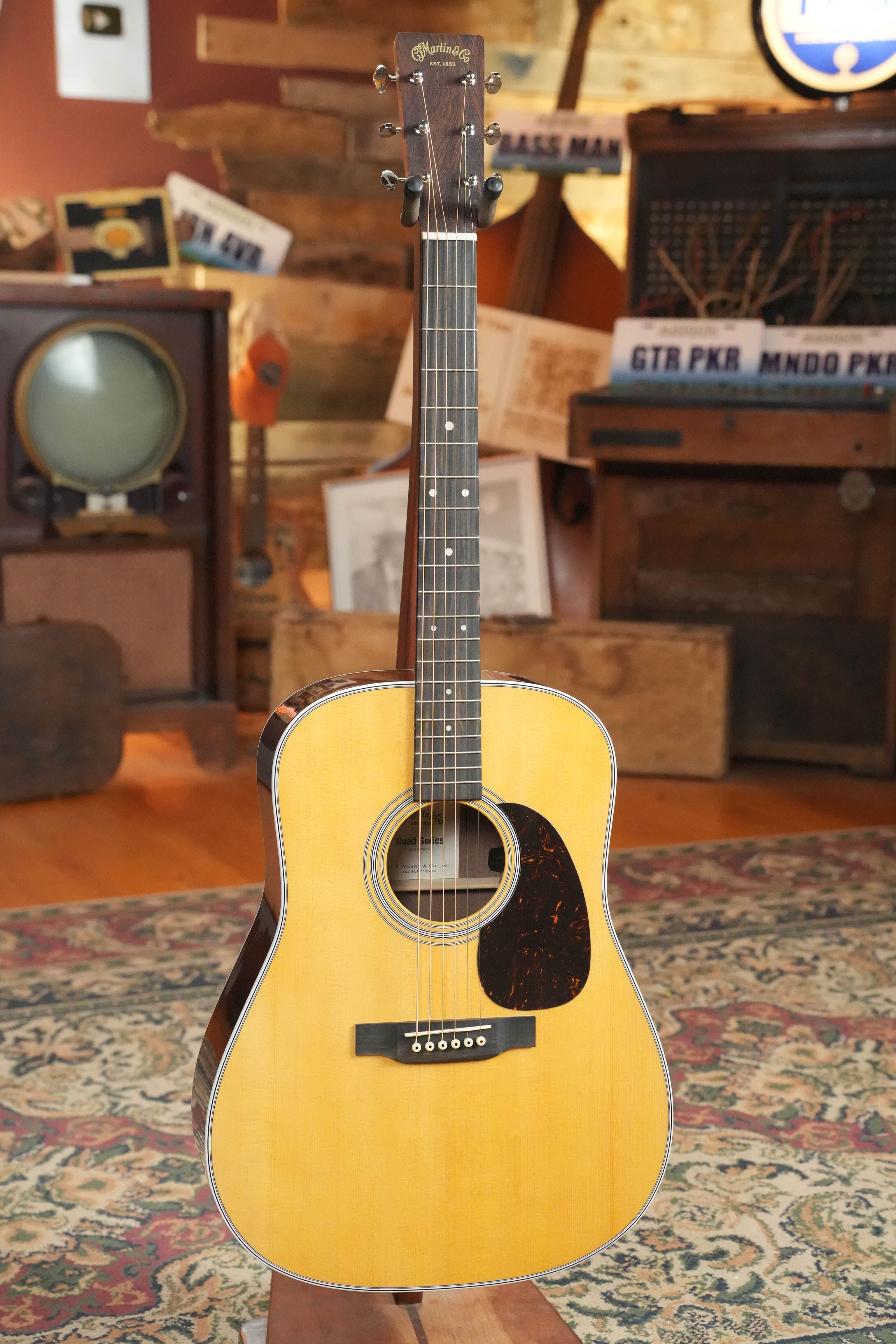 The *New 2026 Model* Martin D-13E Retro Road Series Dreadnought Guitar by Martin & Co., featuring a solid spruce top and natural wood finish, stands on display in a vintage-themed room with a patterned rug and classic decor.