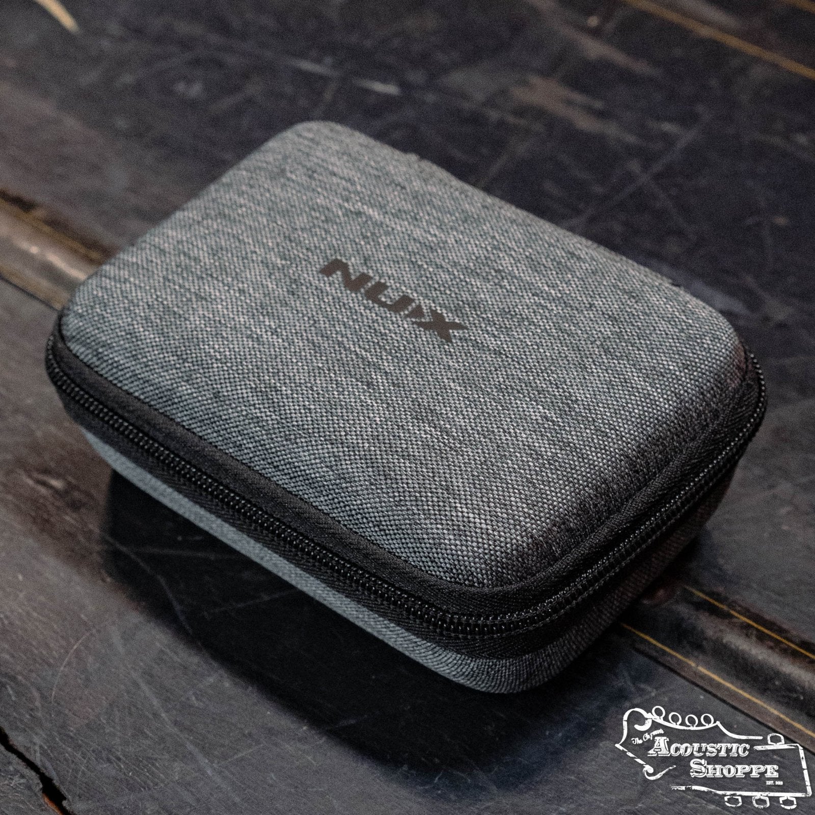 A gray, zippered NUX case for the NUX C-5RC 5.8GHz Wireless Guitar System (Black) rests on a dark wooden surface, featuring a fabric texture, NUX branding on top, and The Acoustic Shoppe logo in the lower right corner.