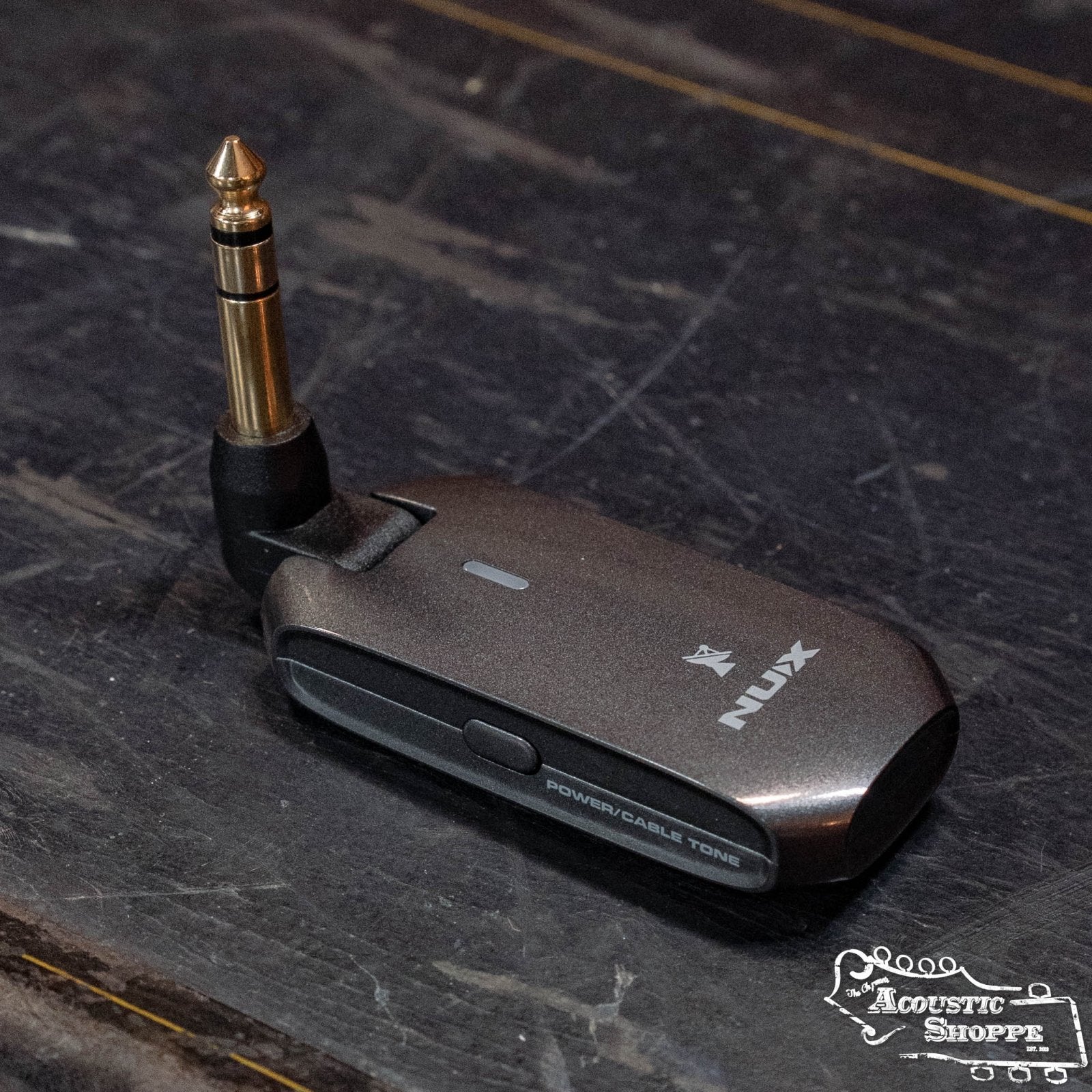 A NUX C-5RC 5.8GHz Wireless Guitar System for Acoustic or Electric Guitar (Black) by NUX, featuring a 1/4-inch plug and labeled POWER/CABLE TONE, rests on a dark surface with The Acoustic Shoppe logo in the bottom right corner.