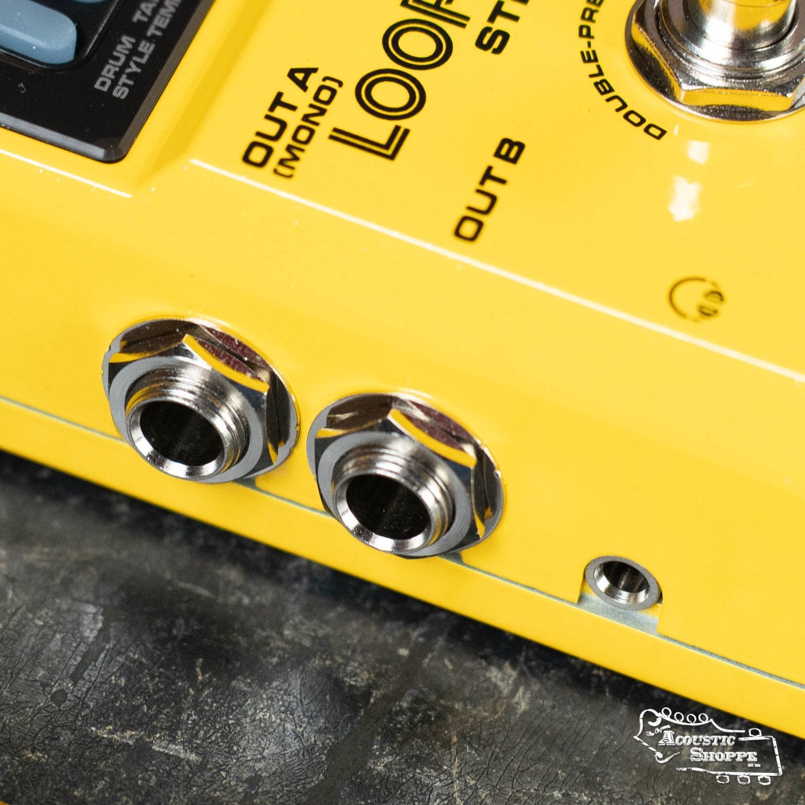 Close-up of the NUX Loop Core Stereo, a yellow guitar effects pedal by NUX featuring stereo looper capability, two audio output jacks labeled OUTA (MONO) and OUT B, part of a footswitch, and the Acoustic Shoppe logo.