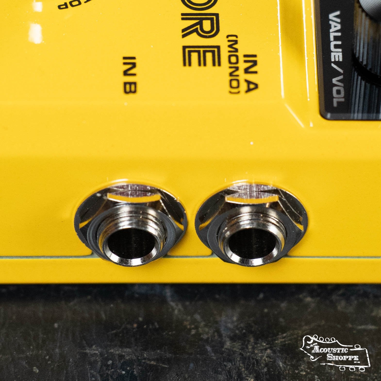 Close-up of a yellow NUX Loop Core Stereo pedal showing two input/output jacks labeled IN A (MONO) and IN B, part of a value/volume control on the right, and the NUX logo at the bottom right.
