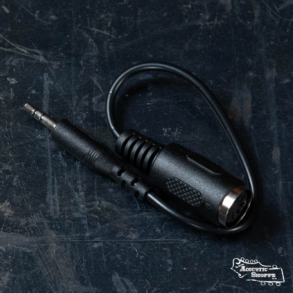 A black NUX audio adapter cable, with a 3.5mm male jack and larger female connector—ideal for connecting the NUX Loop Core Stereo—is shown on a dark textured surface, with The Acoustic Shoppe logo in the bottom right corner.