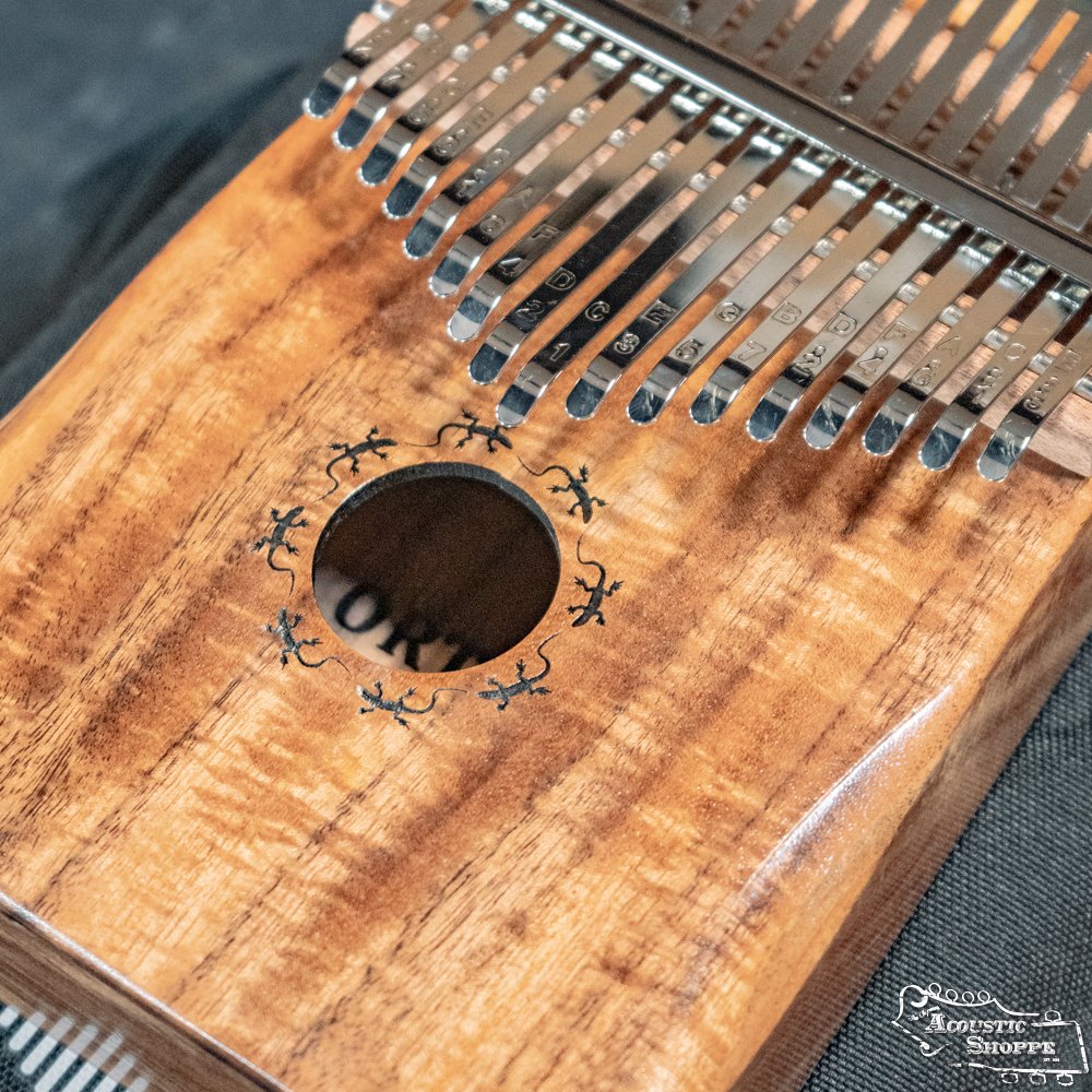 Close-up of the Ortega OKB1 Lizard Series Solid Acacia Wood Kalimba by Ortega, featuring 17 metal tines, a circular sound hole with lizard designs, and detailed corner engraving.