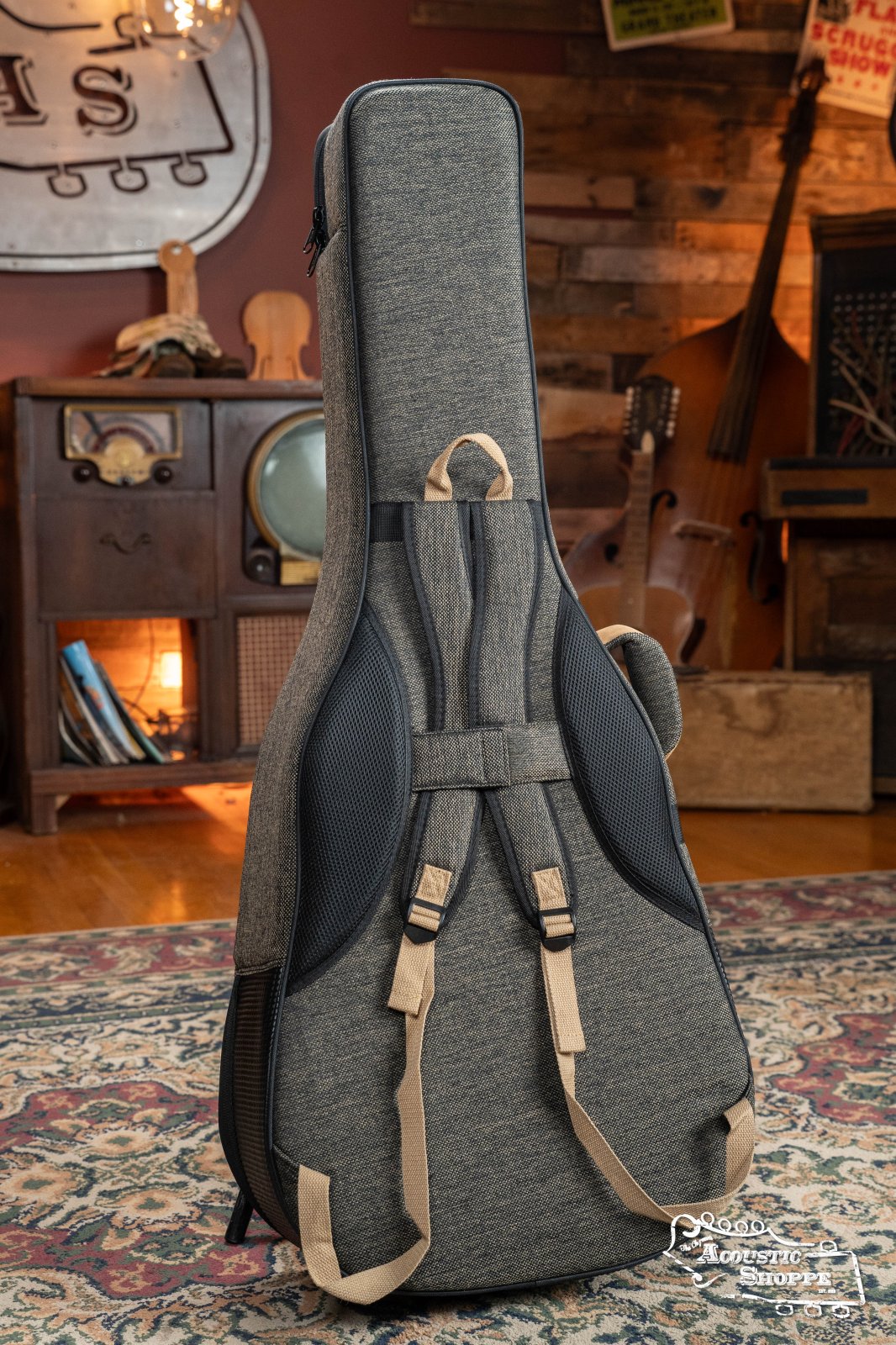 The Ortega OSOCADN-MO Dreadnought Guitar Soft Case in Mocca stands upright on a patterned rug in a cozy, vintage-style room with wooden decor and musical instruments in the background.