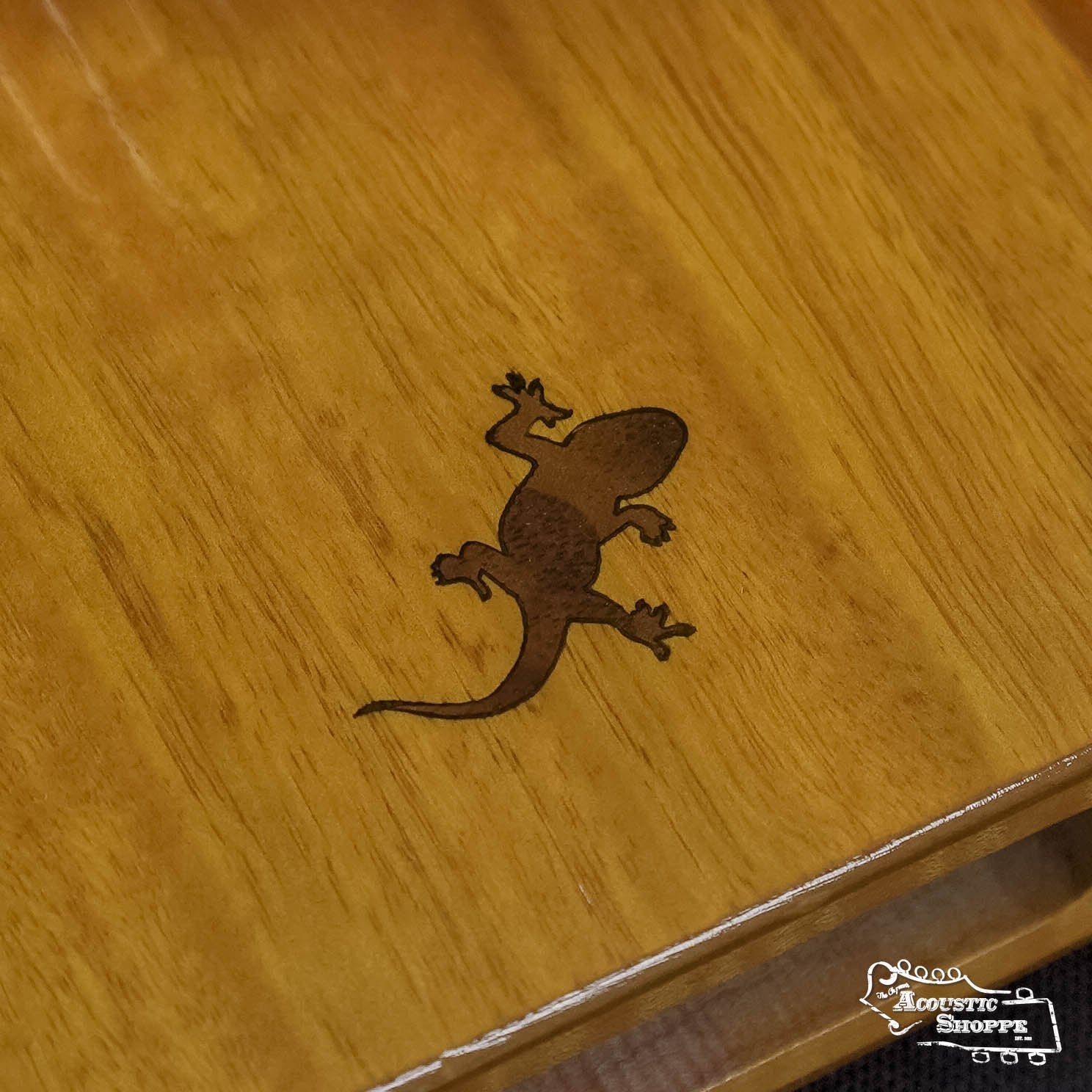 The Ortega OKB3 Lizard Series Solid Golden Phoebe Kalimba features a dark gecko silhouette engraved on its smooth wooden surface, creating a unique and visually striking 17-key C Major instrument.