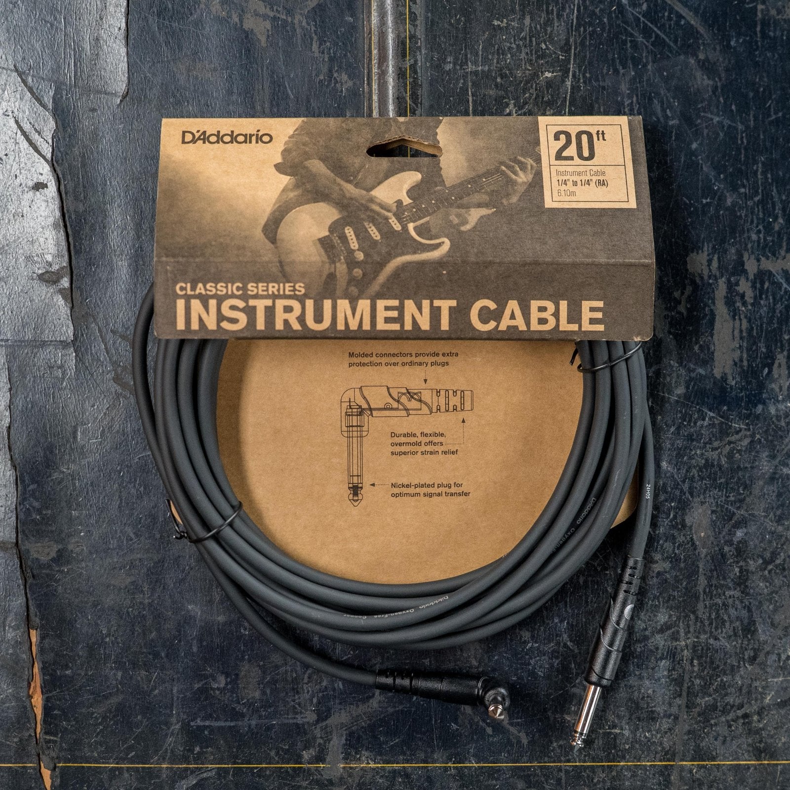 A coiled 20-foot D'Addario PW-CGTRA Classic Series instrument cable (straight to right), in packaging with a brown label and guitar graphic, touts low capacitance and oxygen-free copper, displayed on a dark, worn surface.