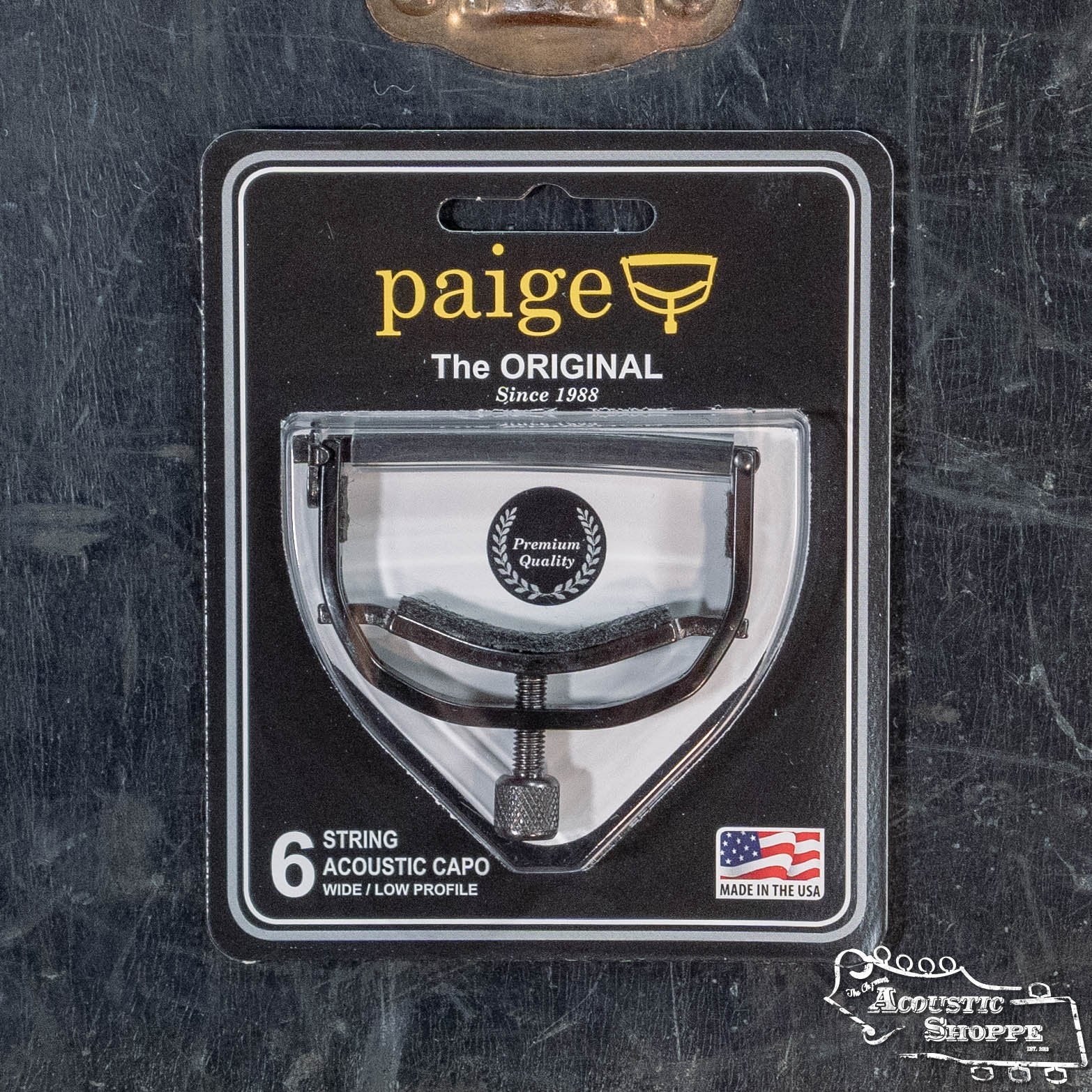 The Paige Original 6-String Acoustic Guitar Capo - Wide/Low Profile (P-6E-W) by Paige Musical Products is packaged with The ORIGINAL, Premium Quality, and Made in the USA highlighted, plus Acoustic Shoppe logo for optimal acoustic fit.