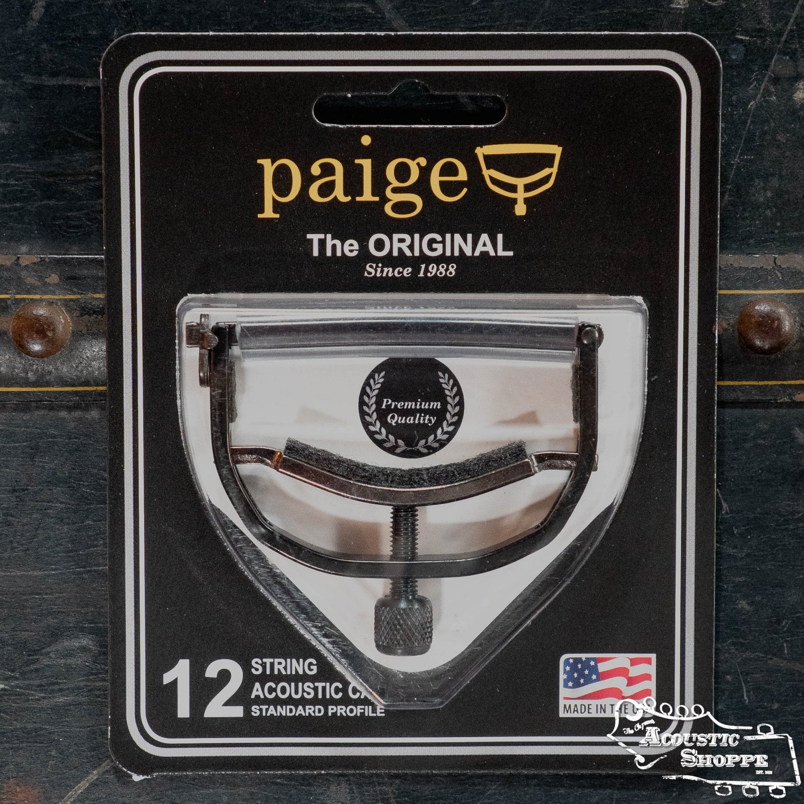 The Paige Musical Products Original 12 String Guitar Capo (P-12E) with Ebony Finish comes in black packaging with gold and white text, featuring a Premium Quality badge and a small American flag in the bottom right corner.