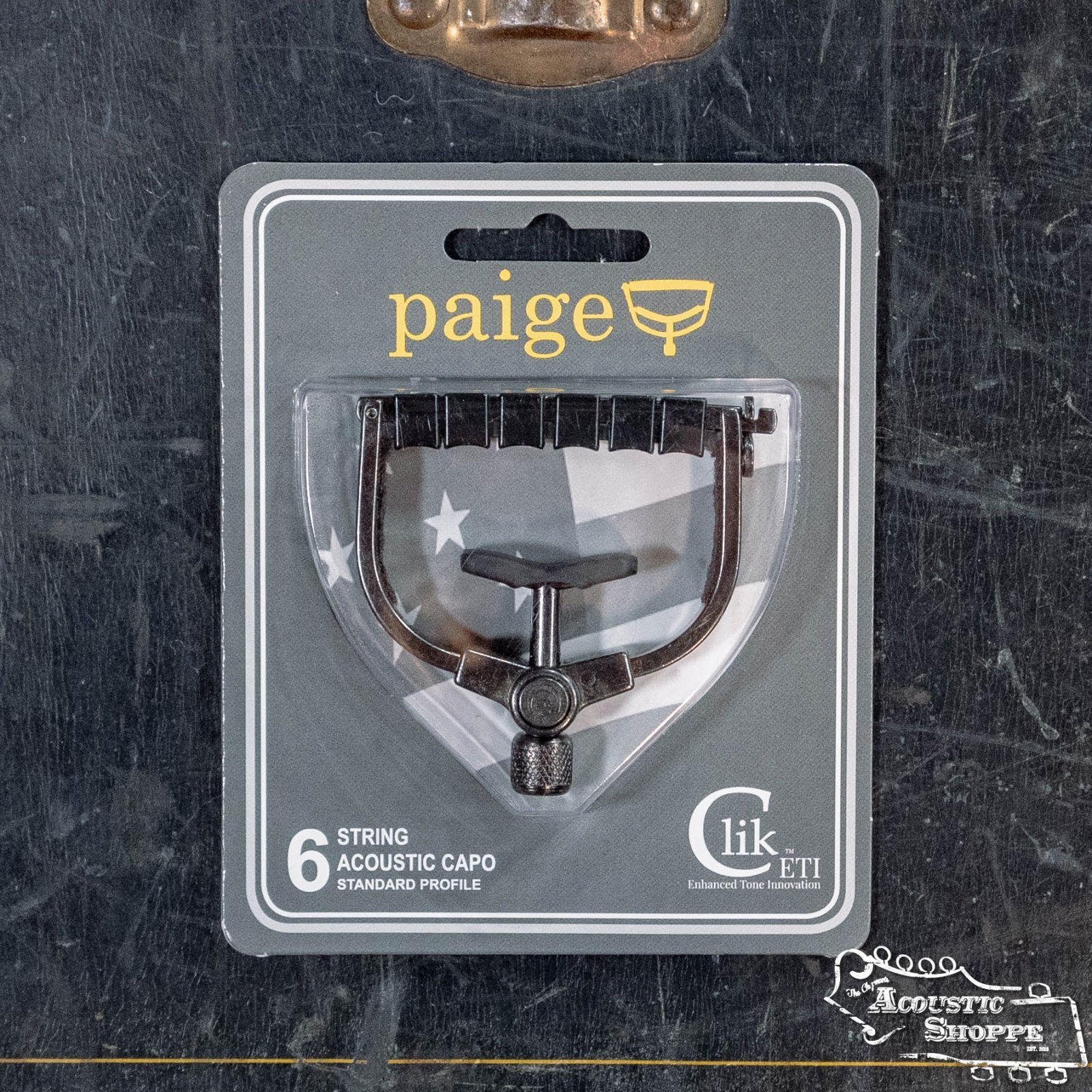 The Paige Musical Products Click ETI 6-String Acoustic Guitar Capo (PC-6-ETI), labeled Standard Profile, is displayed in its packaging against a dark background with The Acoustic Shoppe logo in the bottom right corner.