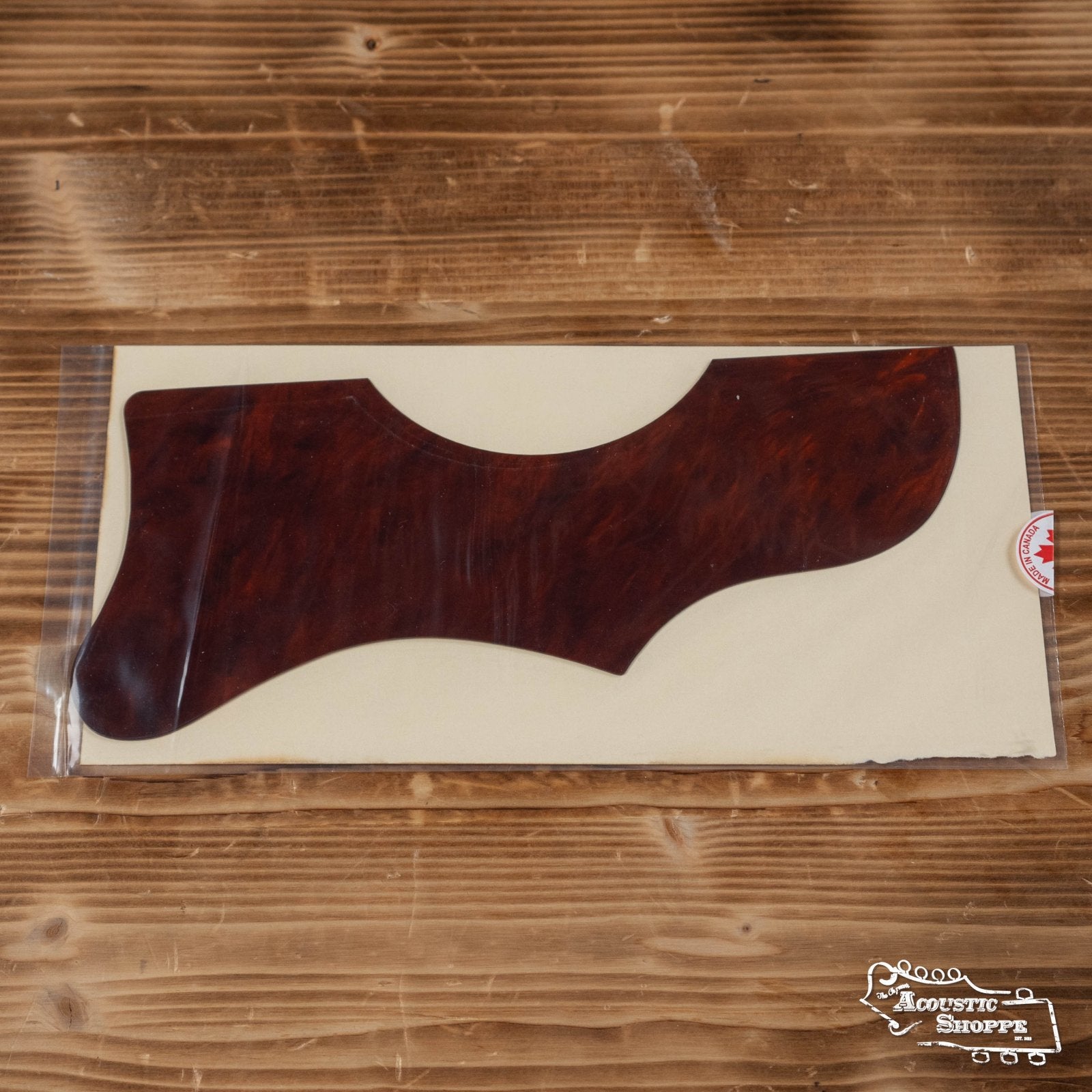 A Proulx Lutherie Tortoloid RD-Long J45 Hand-Poured Custom Pickguard with a tortoiseshell pattern, in clear packaging on a light surface over wood. The Acoustic Shoppe logo appears at the bottom right.