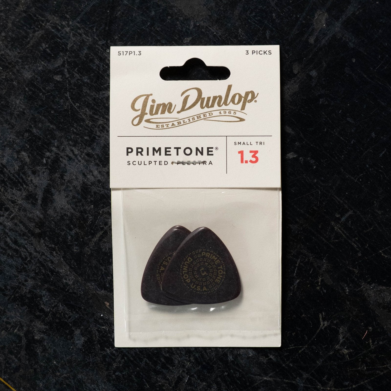 The Dunlop Primetone Small Triangle Smooth Pick 3 Pack - 517P 1.3 Gauge features three dark picks in white, black, and gold packaging, crafted for precision and comfort.