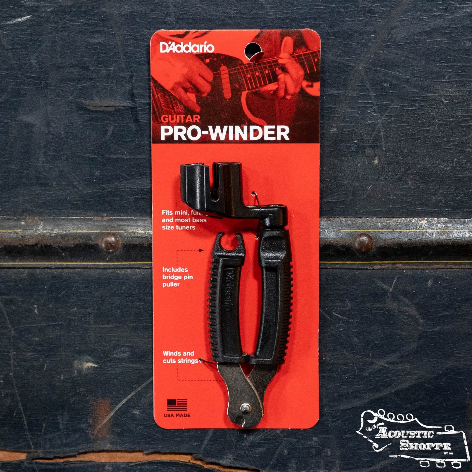 The D'Addario Pro-Winder String Winder and Cutter in black comes on a red card. The package shows a hand playing guitar and highlights winding, string cutting, and pin pulling—ideal for restringing. Brand: D'Addario.