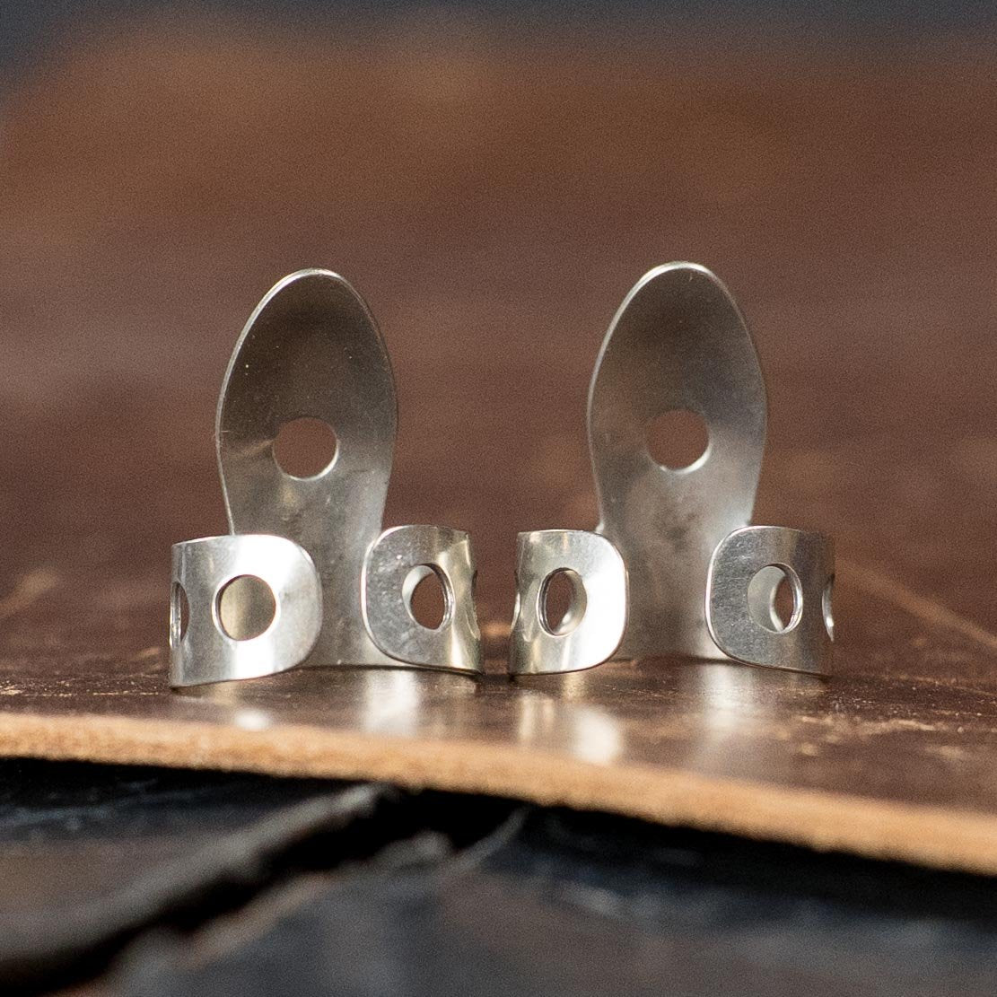 Two shiny ProPik Heritage Fingerpicks (2-Pack, 11-209-4000) stand upright side by side on a brown leather surface.