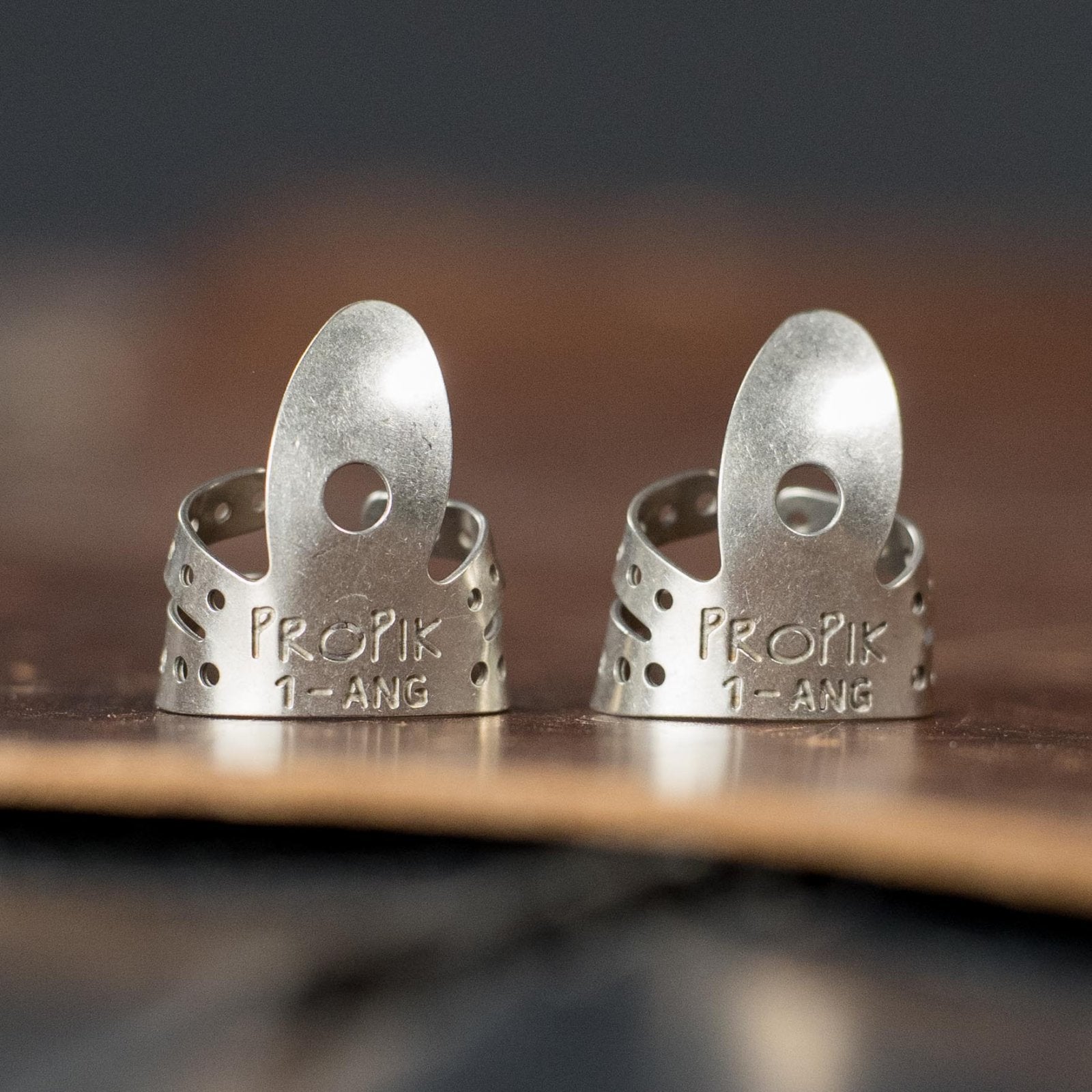 Two ProPik Angled Extra Comfortable Nickel Split Wrap #1 Finger Picks (2-pack) stand upright on leather, showing ventilated bands and curved blades ideal for playing stringed instruments.