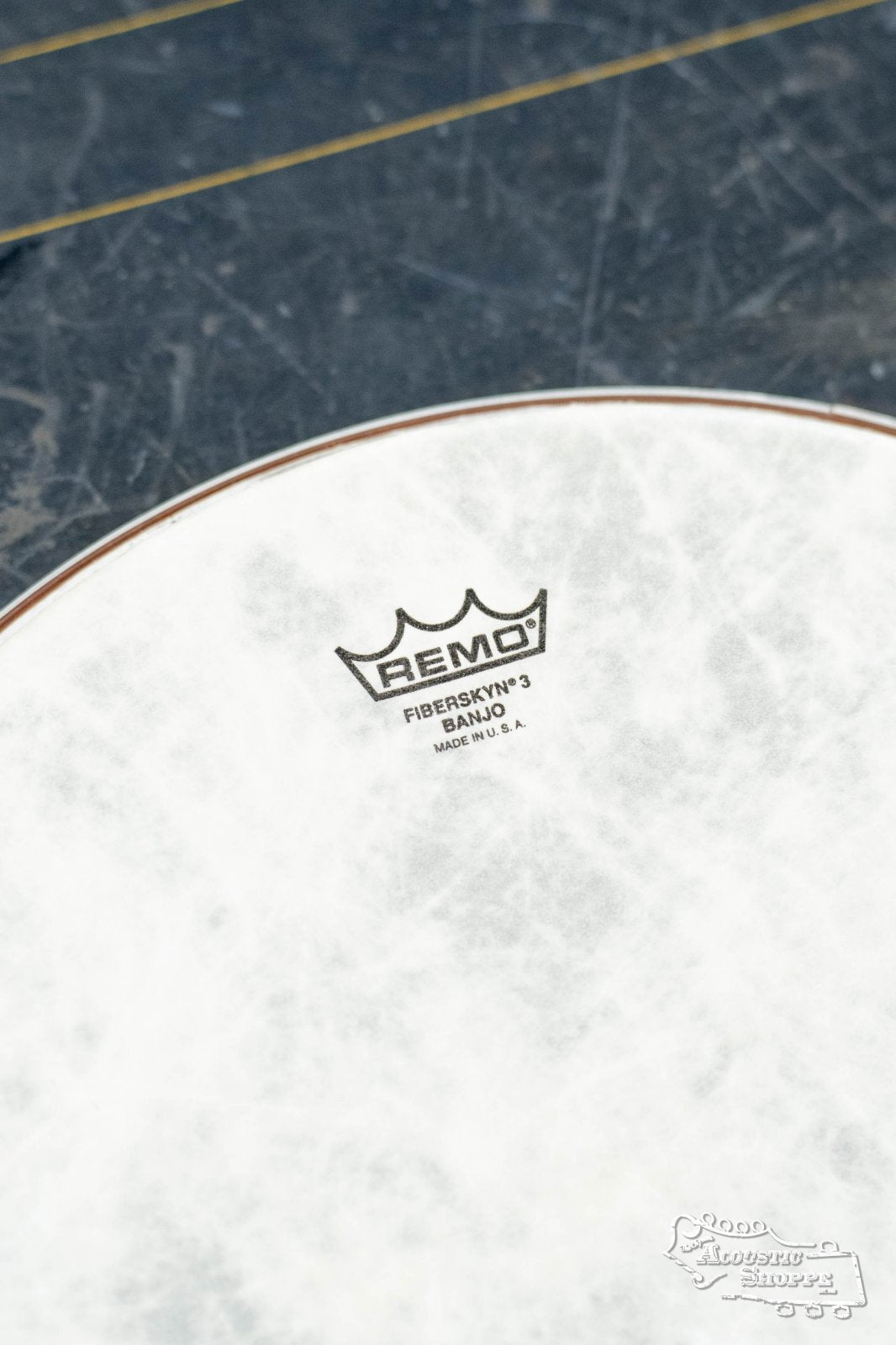 Close-up of a Remo Banjo Fiberskyn Medium Collar 10-11/16in drumhead with brand logo and textured white surface, shown on a dark marbled background.