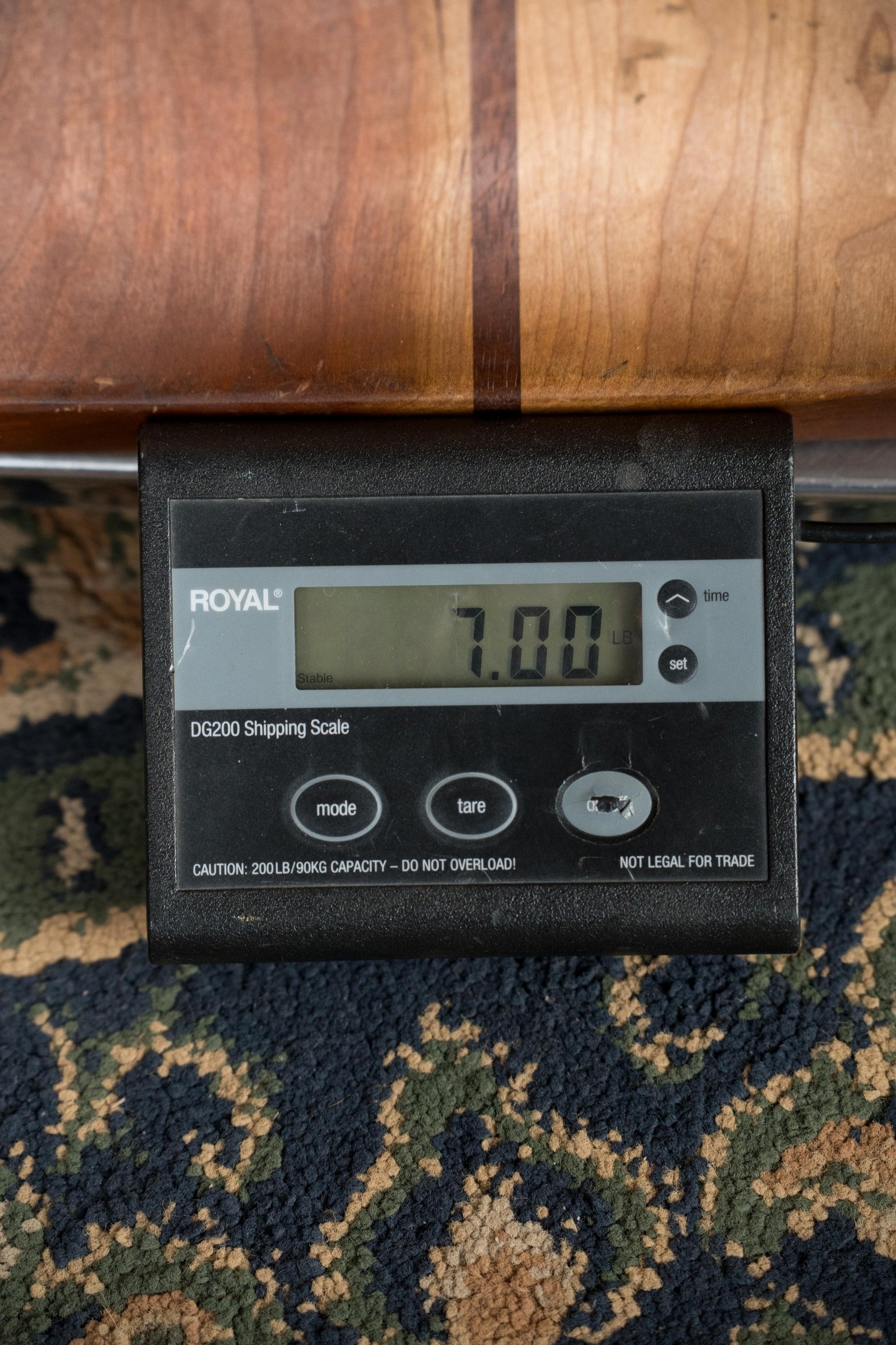A digital shipping scale shows 7.00 pounds as it supports a Recording King RKH-05 Dirty 30s Resonator Banjo #2563 by Recording King, resting on a patterned carpet.
