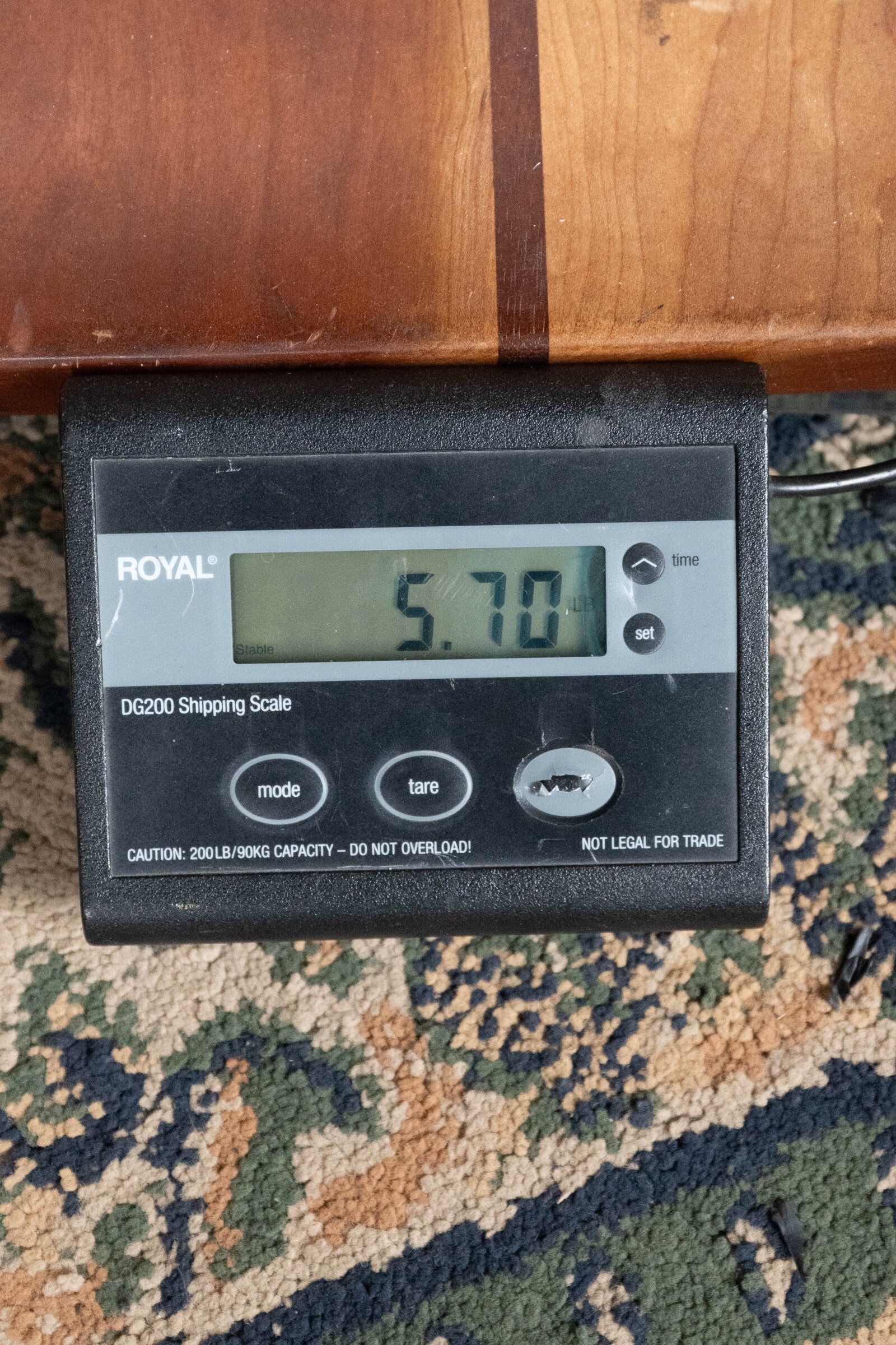 A digital shipping scale on a patterned carpet reads 5.70 pounds. Above the scale, part of a Recording King RR-36S-VS All Mahogany Vintage Sunburst Square Neck Resonator Maxwell Series #6003 is visible.