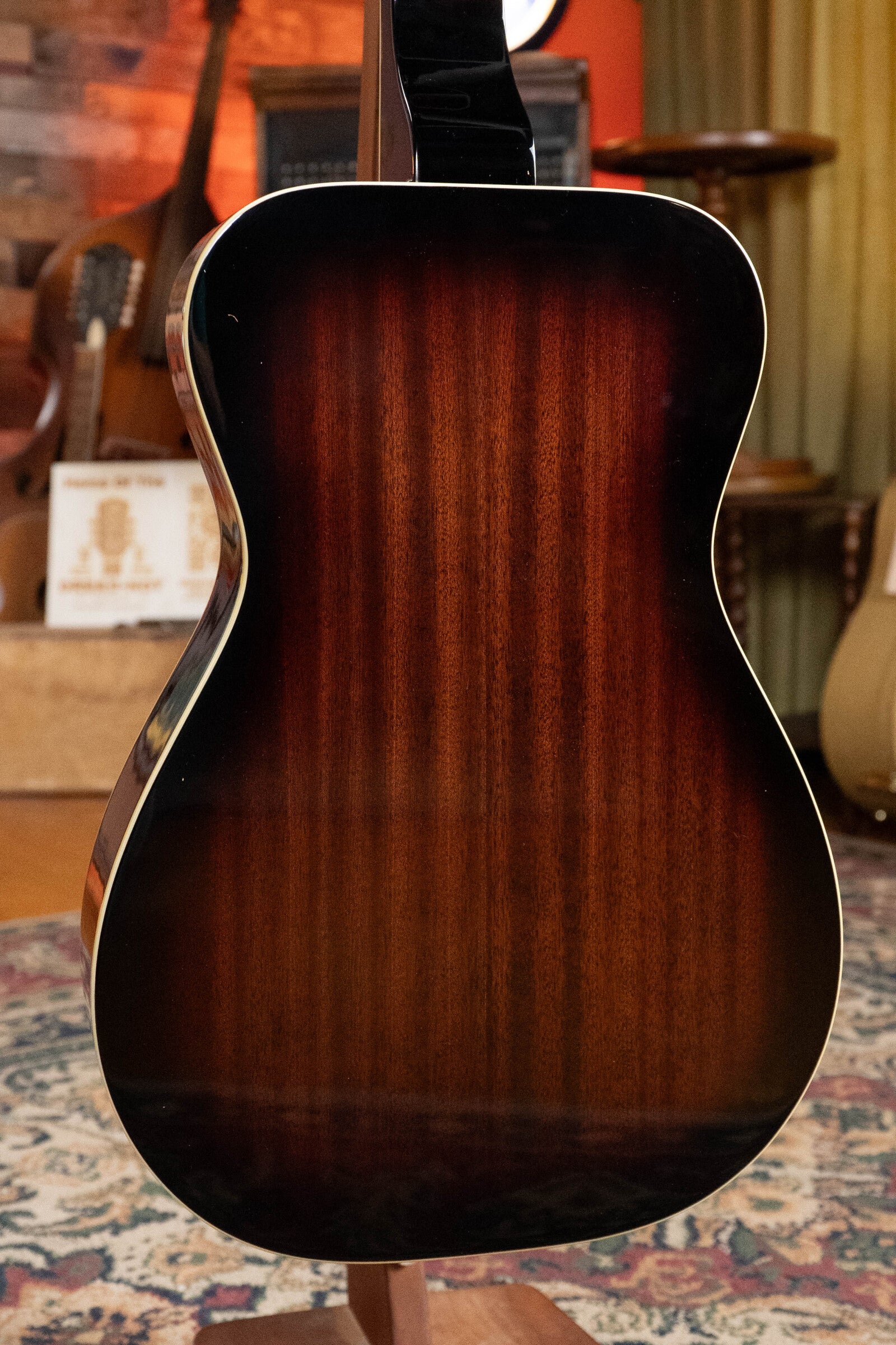 The Recording King RR-36S-VS All Mahogany Vintage Sunburst Square Neck Resonator (Maxwell Series #6003) features a rich sunburst finish with a dark-to-light brown gradient, set in a cozy room with instruments and warm decor, by Recording King.