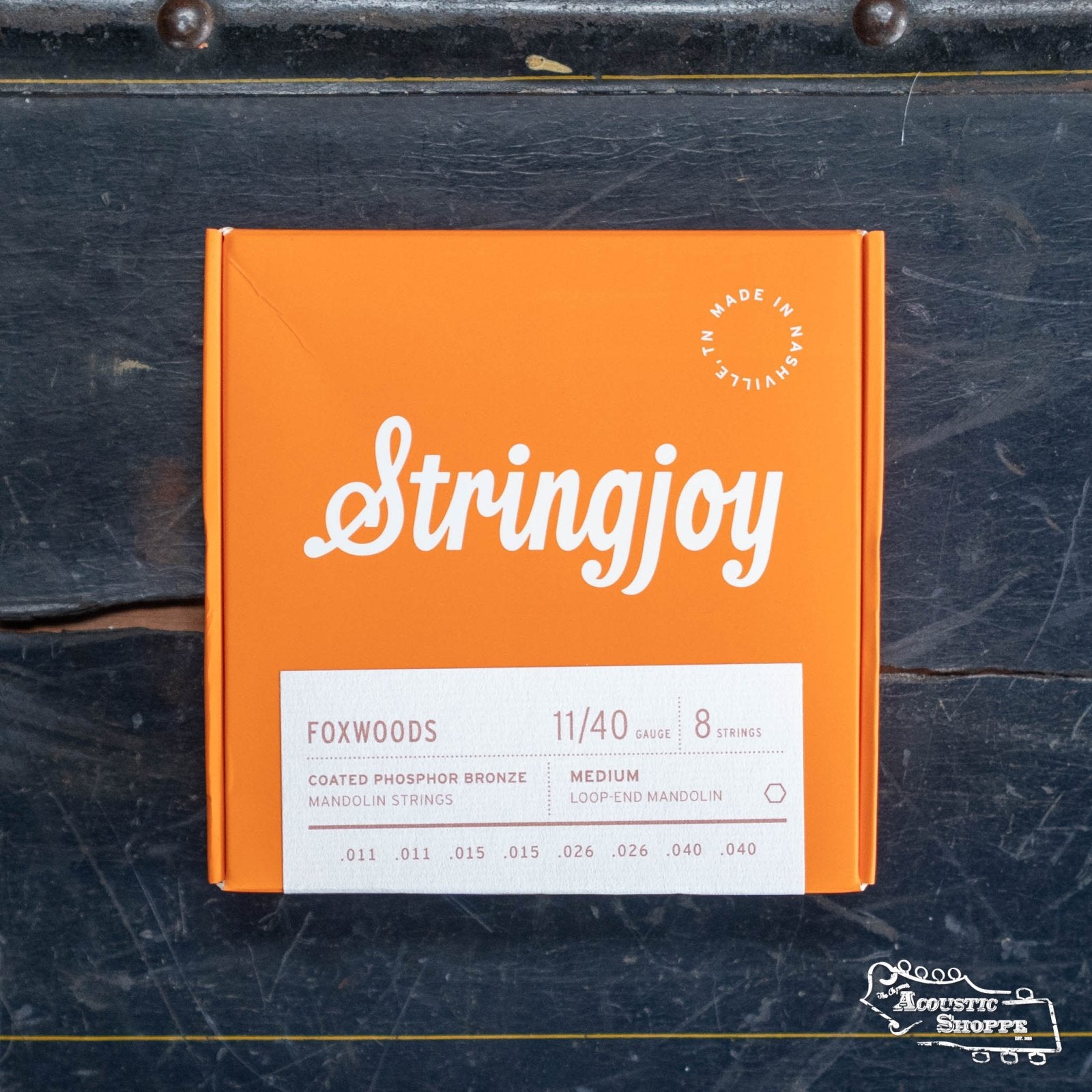A Stringjoy Mandolin Foxwoods Medium Gauge (11-40) Coated Phosphor Bronze Strings box sits on dark wood, displaying “Made in Nashville” and the Acoustic Shoppe logo.