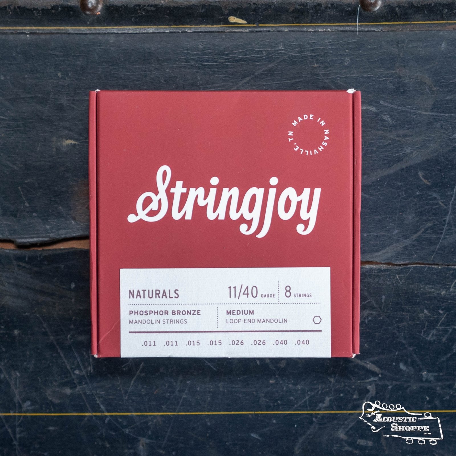 A red Stringjoy Mandolin Naturals Medium Gauge (11-40) Phosphor Bronze Strings box with 8 premium loop-end strings rests on a dark wooden surface.