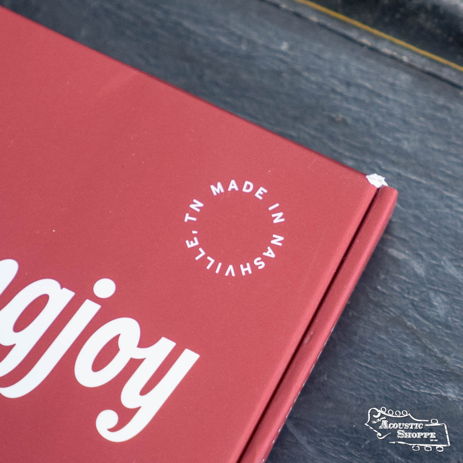 A partially visible red Stringjoy Mandolin Naturals Medium Gauge (11-40) Phosphor Bronze Strings box with white text and a MADE IN NASHVILLE, TN stamp sits on a dark surface; the Acoustic Shoppe logo appears at bottom right.