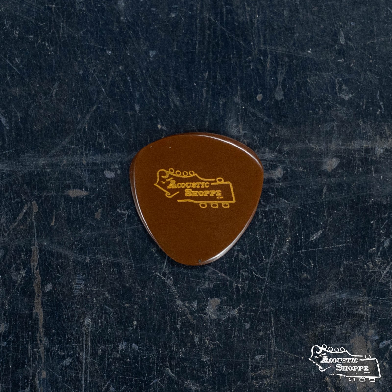 A BlueChip Picks (SR60) guitar pick by BlueChip, precision machined for quality, showcases a yellow guitar headstock outline and branding—resting on a worn, dark-textured surface—ideal for boutique pick enthusiasts.