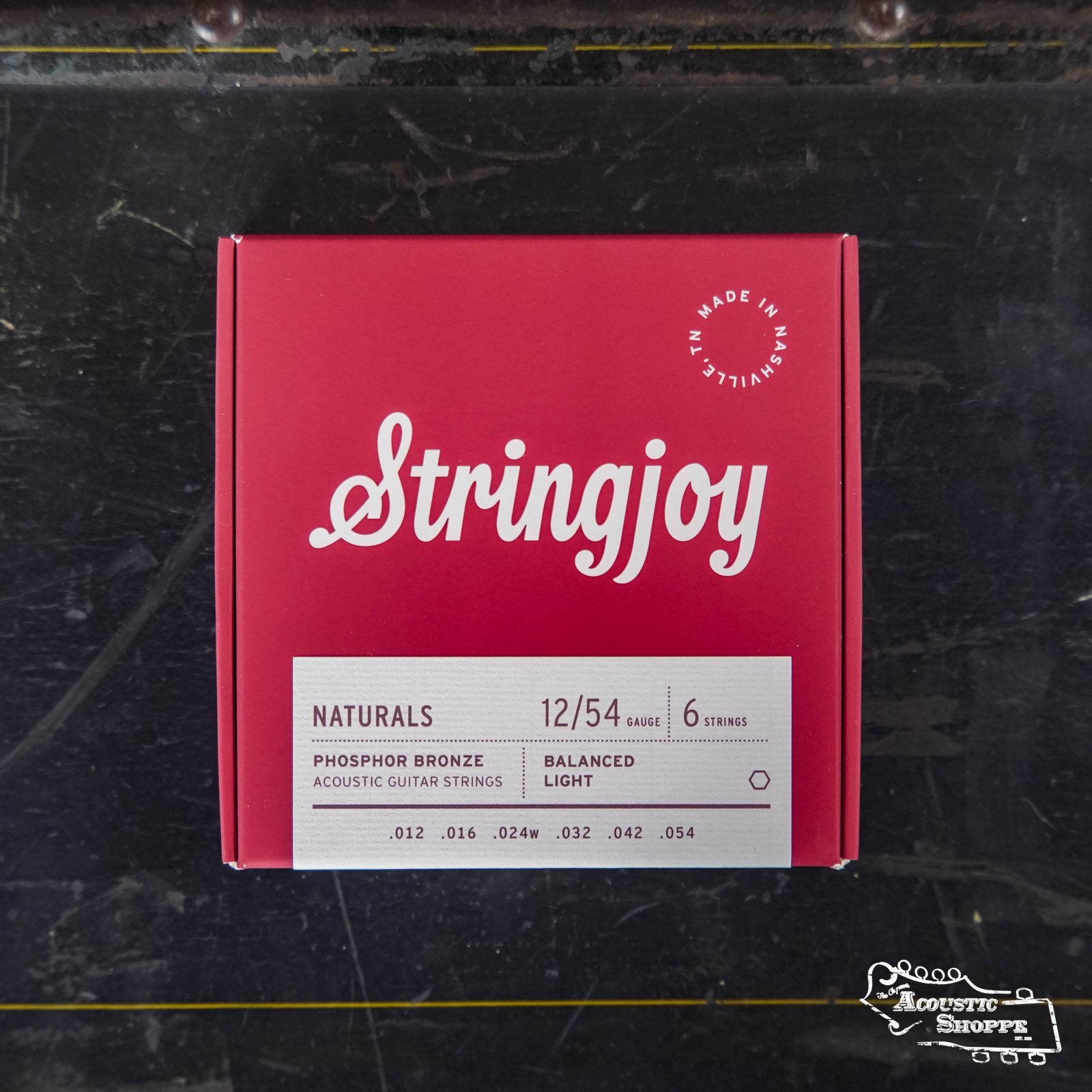 A red box of Stringjoy Naturals Light Gauge (12-54) Phosphor Bronze Acoustic Guitar Strings sits on a dark surface, showing six strings and “Made in Nashville” printed on the label.