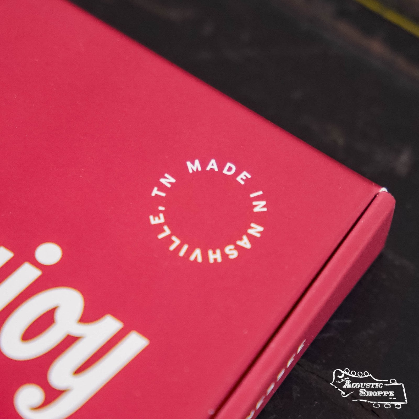 A close-up of a red Stringjoy Naturals Medium Gauge (13-56) Phosphor Bronze Acoustic Guitar Strings box shows MADE IN NASHVILLE, TN in a white circle and part of enjoy, with the Acoustic Shoppe logo in the bottom right corner.