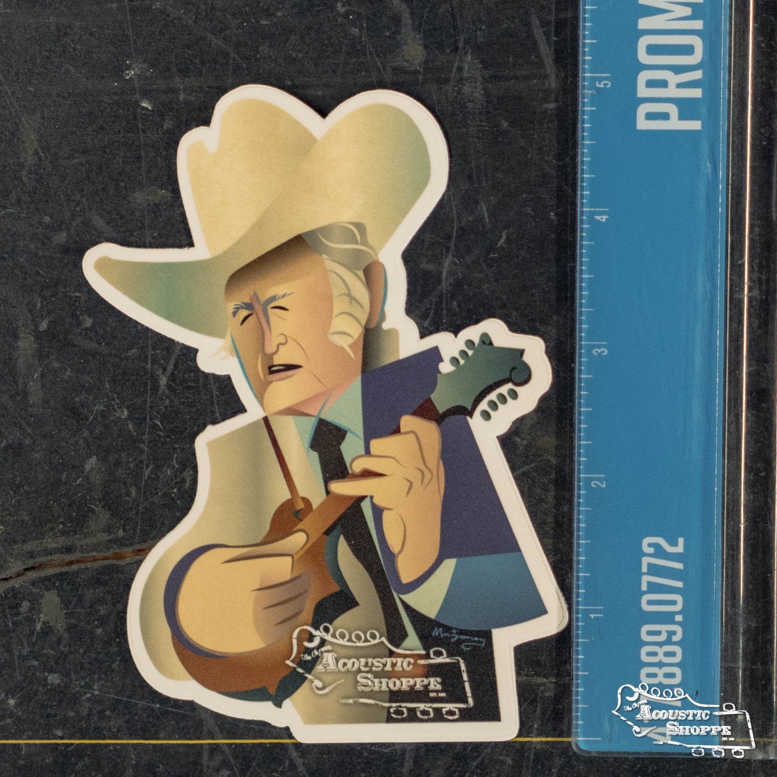 The Bill Monroe Sticker by Mark A Montgomery features a cartoon man in a cowboy hat with mandolin, beside a blue ruler. The Acoustic Shoppe branding at the bottom highlights quality boutique acoustic instruments.