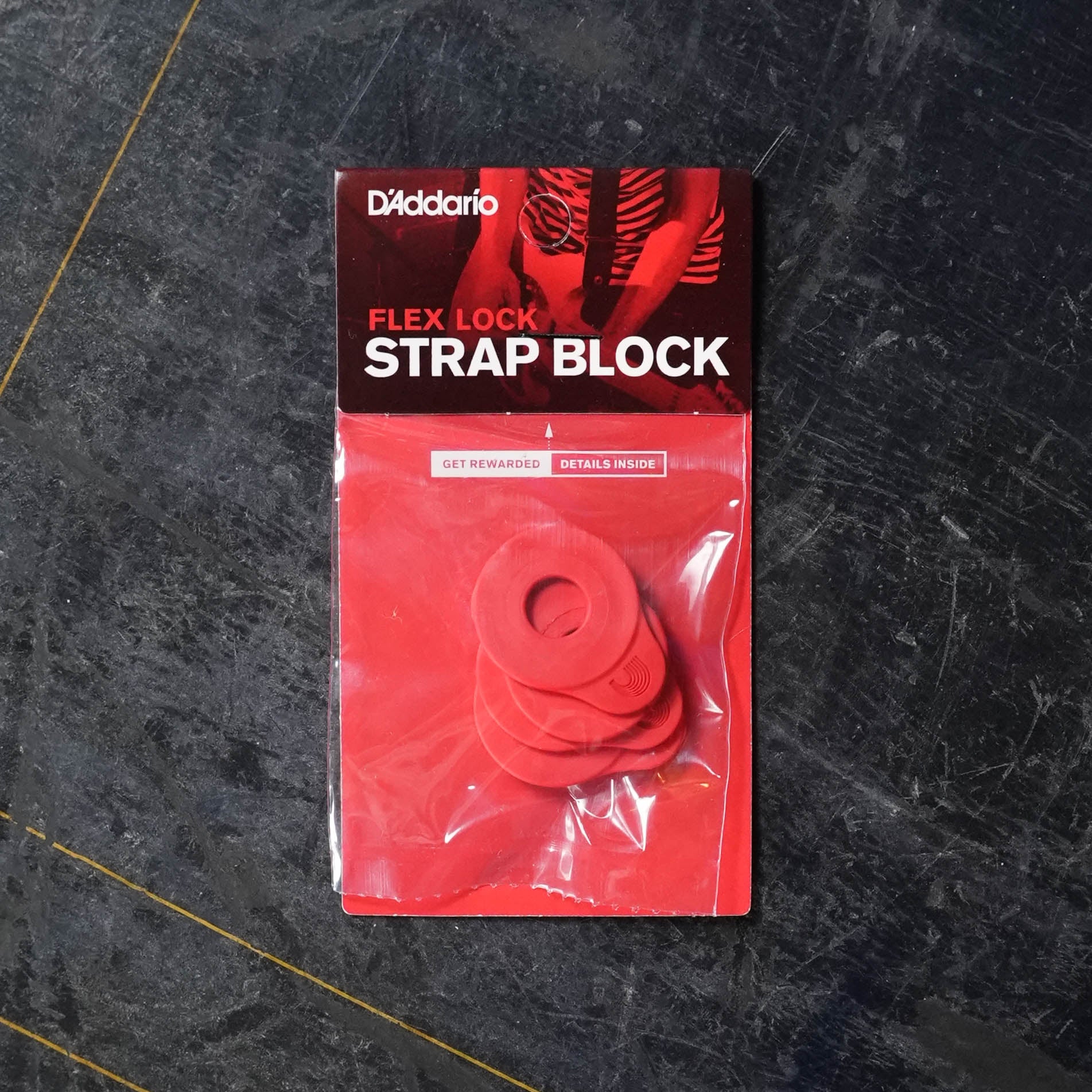 A D'Addario Flex Lock Strap Block 4-Pk - Red, featuring four red strap locks for guitar end pins, is displayed on a dark, textured surface.