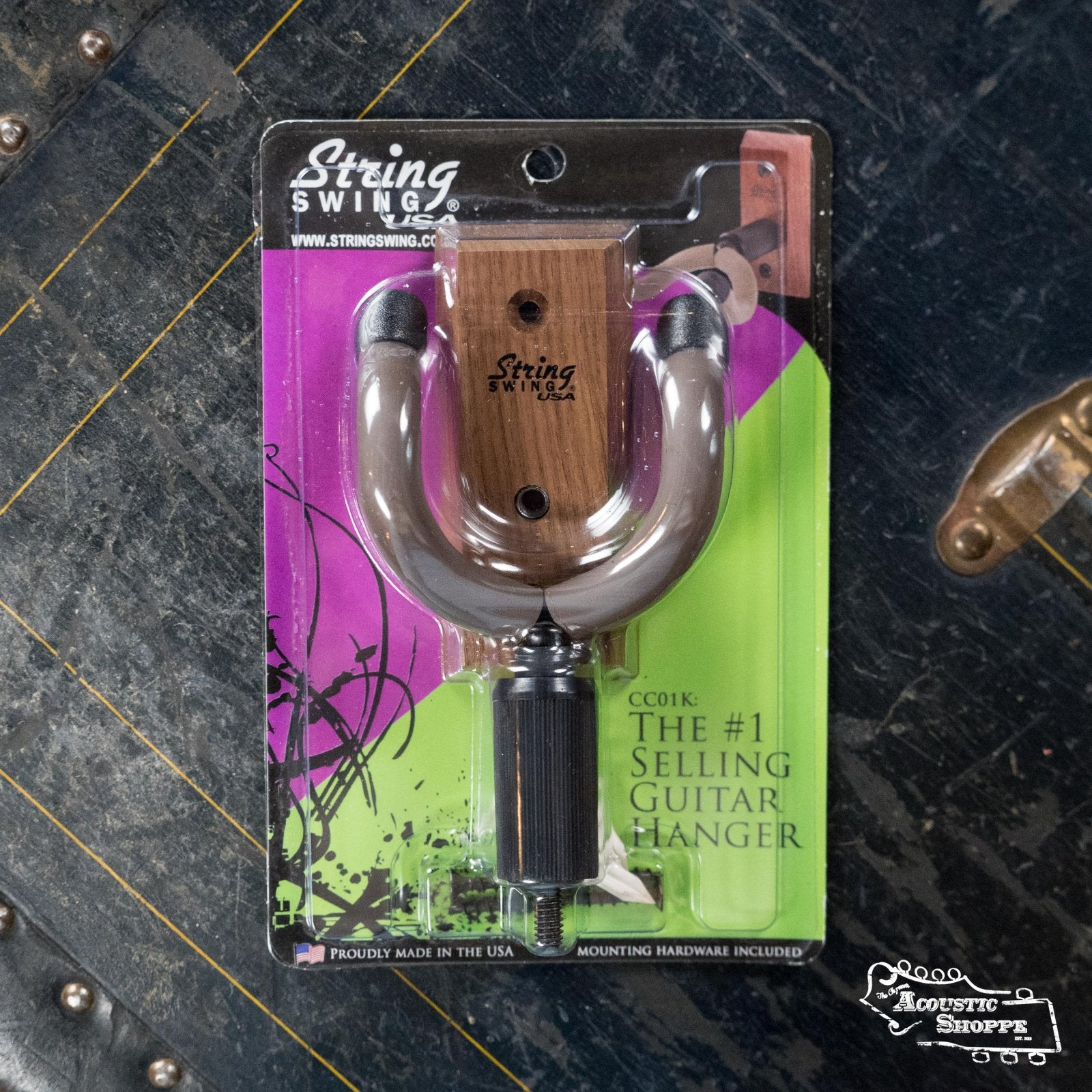 A String Swing Home & Studio Guitar Hanger, with a wooden base and metal hook, is shown packaged on a dark surface with The Acoustic Shoppe logo in the bottom right corner.