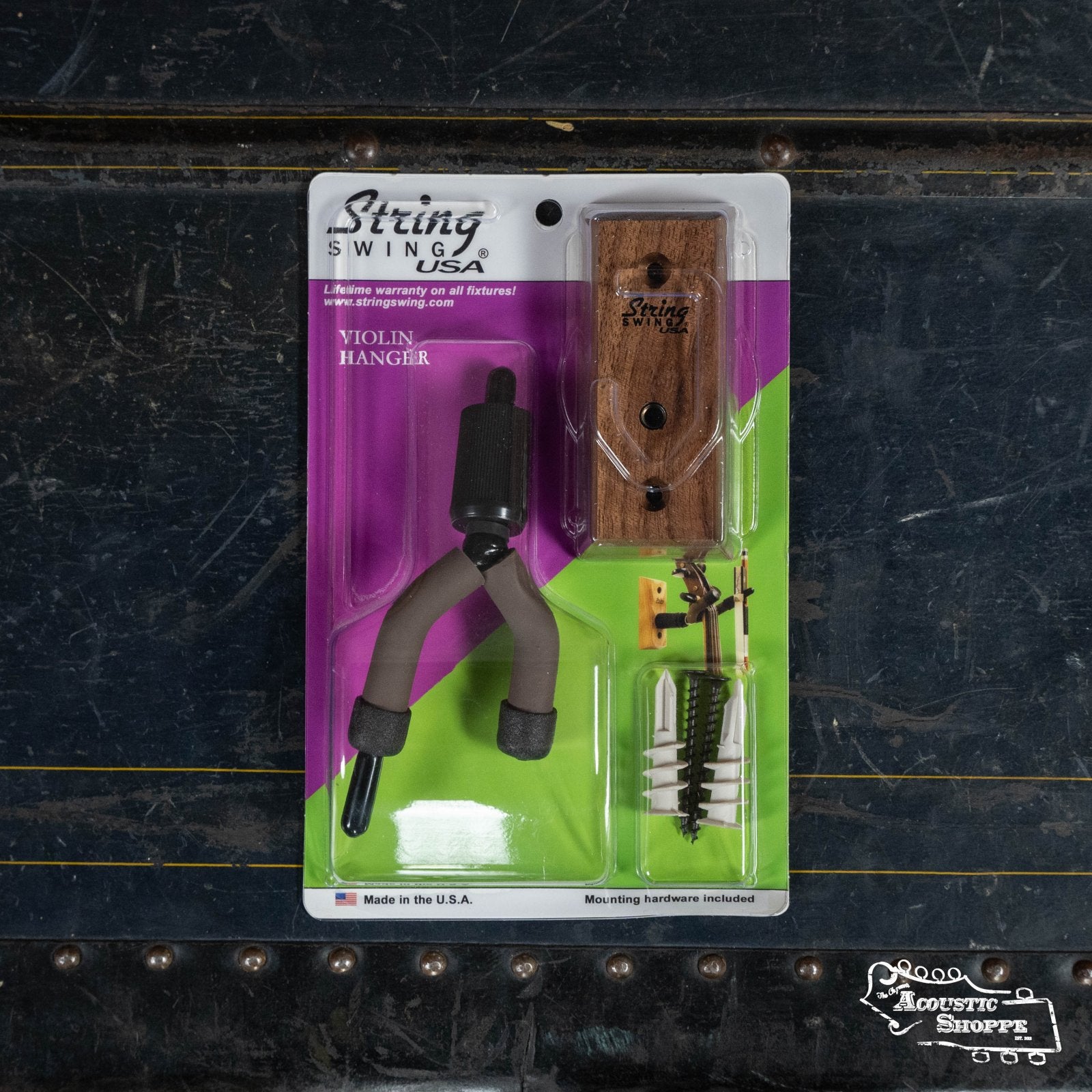 Packaged String Swing Black Walnut Home & Studio Violin Hanger (CC01V-BW) with mounting hardware rests on a textured black surface. The branded packaging has purple and green accents and displays a padded hardwood violin holder.