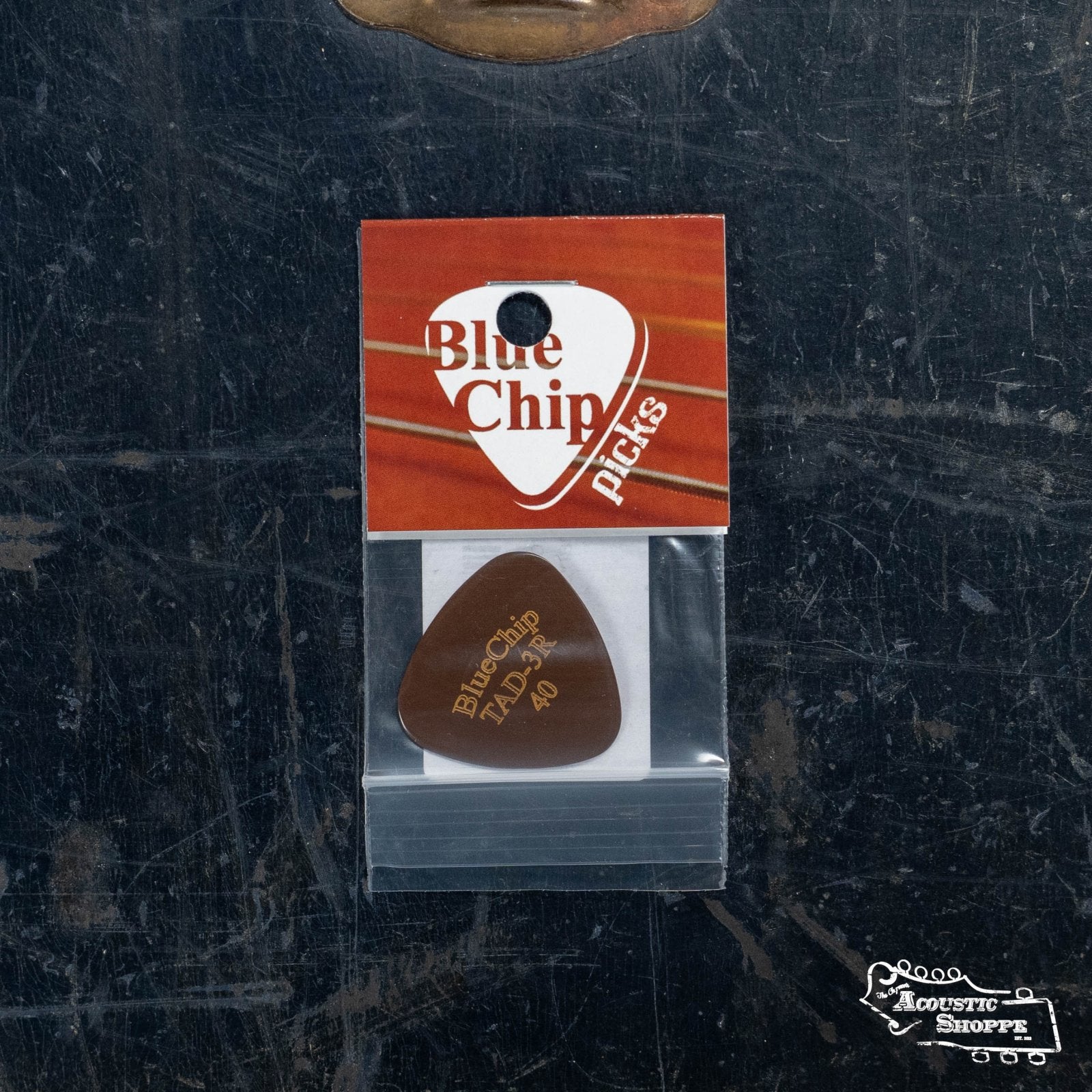 A BlueChip Picks (TAD40-3R) guitar pick by BlueChip in a clear plastic bag with branded label, set on a dark textured surface featuring The Acoustic Shoppe logo—ideal for acoustic music accessory enthusiasts.