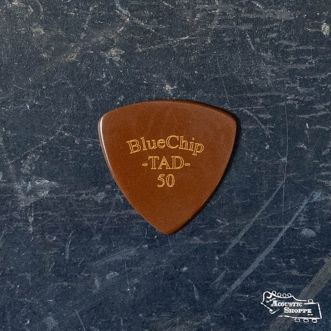 The BlueChip Picks (TAD50) by BlueChip rests on a dark, textured surface with a white “Acoustic Shoppe” logo in the corner—highlighting this premium pick as a must-have acoustic accessory.