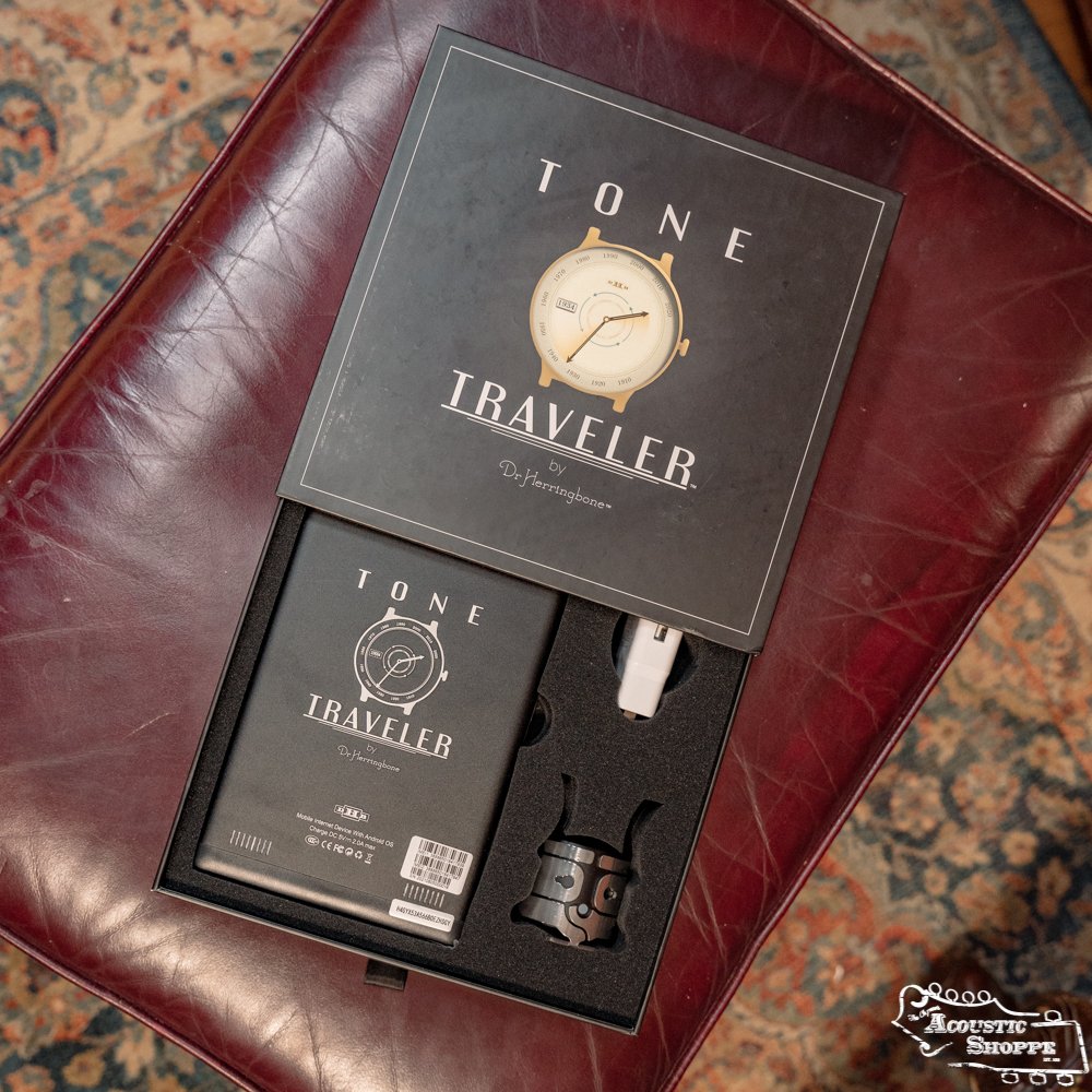 The DrHerringBone Tone Traveler Trio Package rests on red leather, its open box revealing a booklet, an acoustic enhancement device, and accessories, all neatly organized in custom foam.