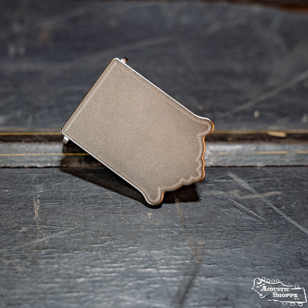 The James Nickel Traditional Mandolin Tailpiece by Axiom Inc., shaped like the outline of Oklahoma, rests on a textured dark surface.