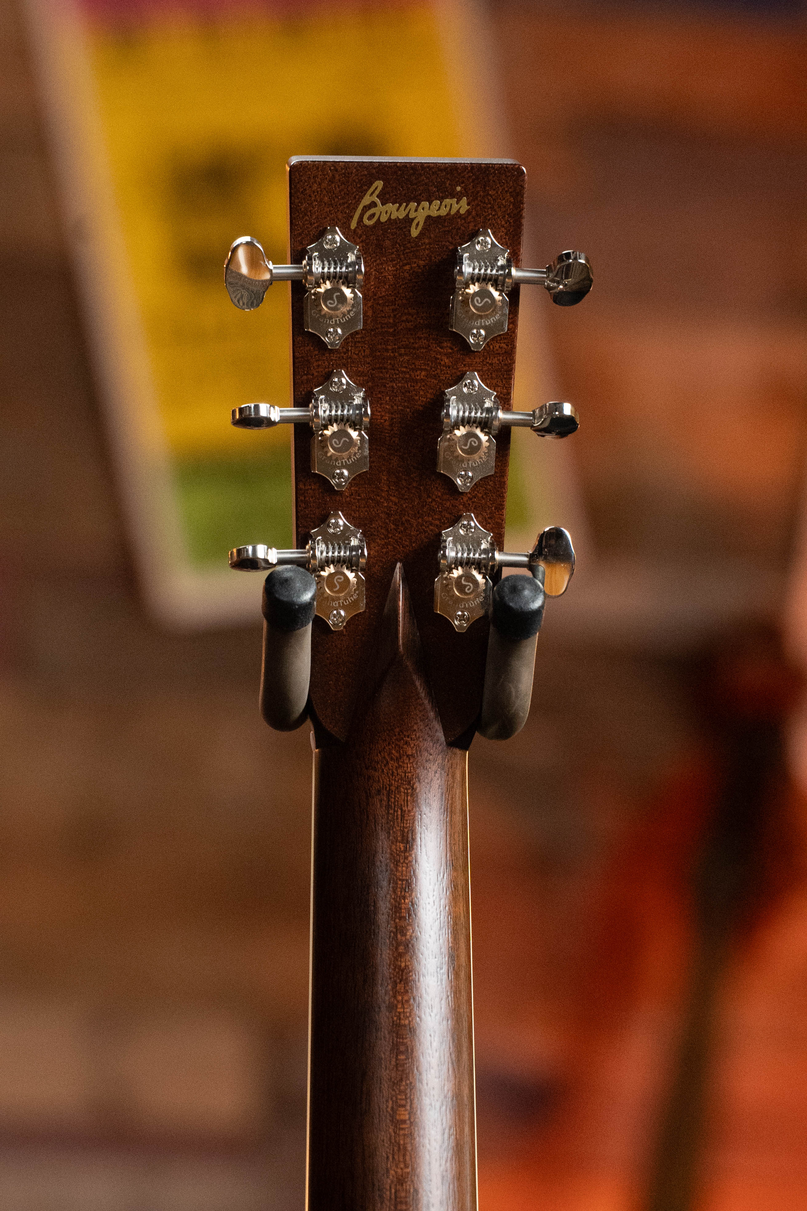 Close-up of the Bourgeois TAS LSH Professional Series Satin Dreadnought Guitar headstock with six tuning pegs and the Bourgeois logo, against a blurred warm background. *Pre-Order 25% Deposit ONLY*.