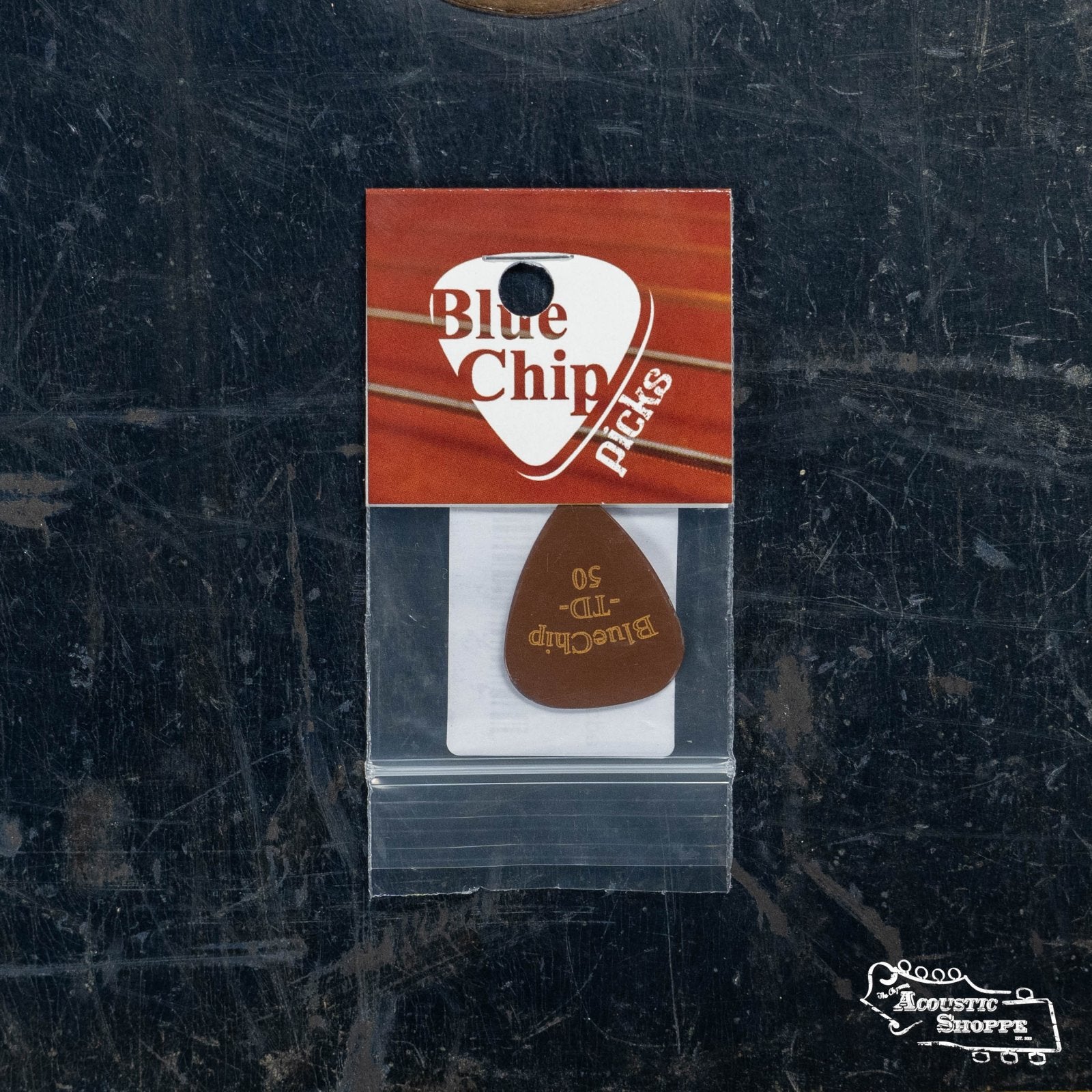 A BlueChip Picks (TD50) teardrop guitar pick by BlueChip, packaged in a clear bag with branded card, rests on a dark surface with an Acoustic Shoppe logo—ideal for fans of premium acoustic music accessories.